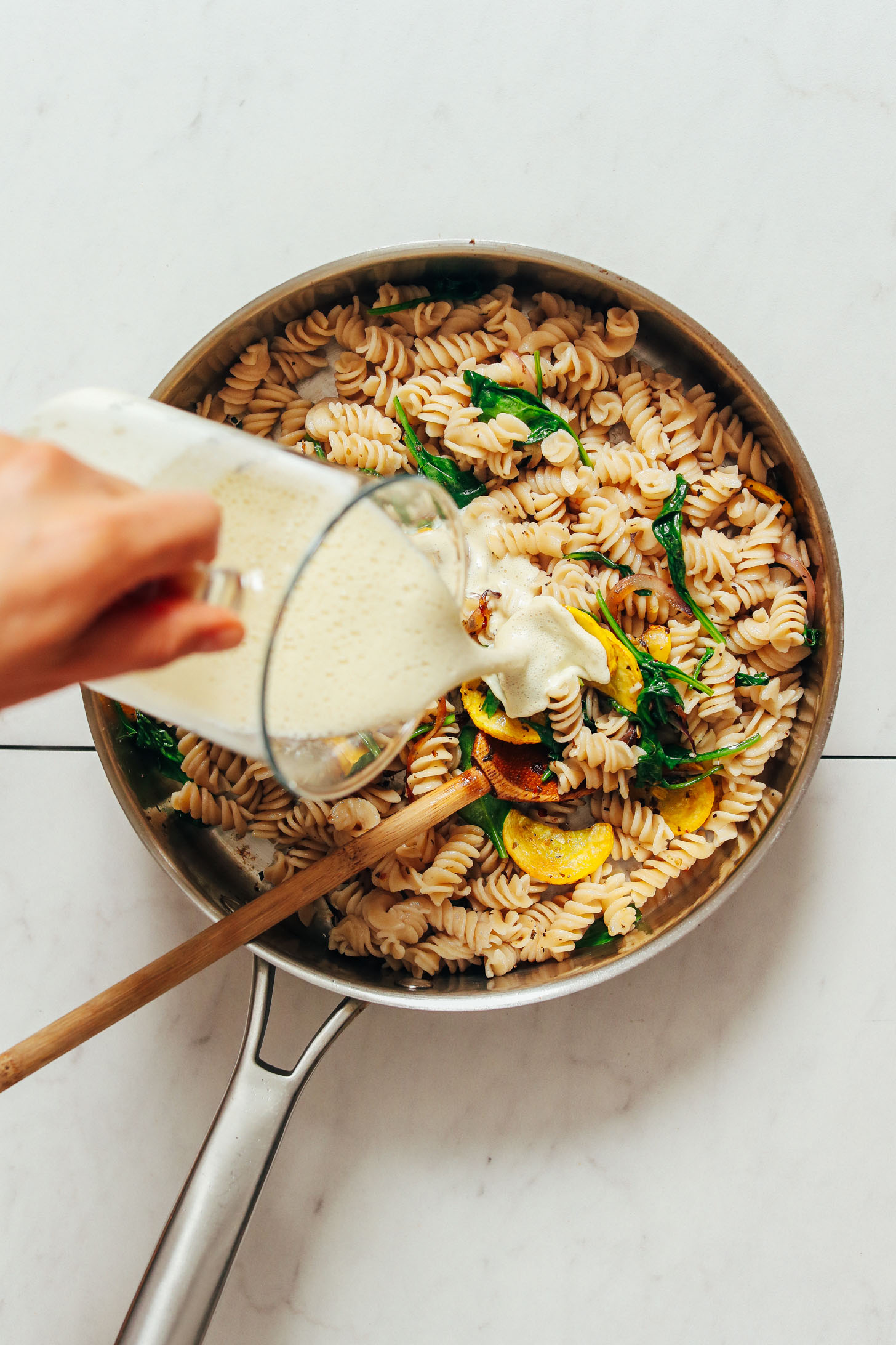 Pouring creamy cashew alfredo onto pasta and sautéed veggies