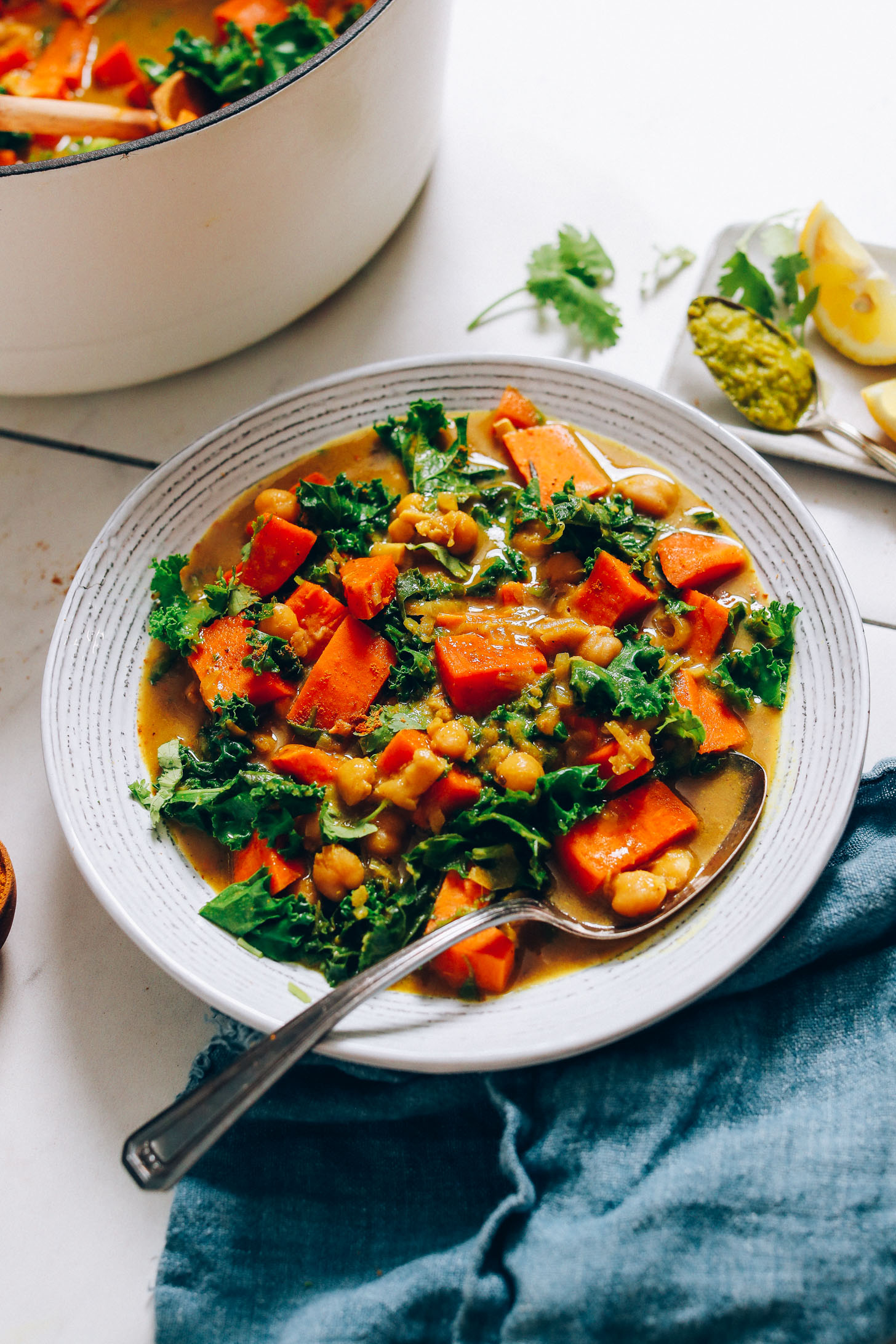 Vintage spoon holding sweet potatoes and chickpeas in a bowl of vegan Green Curry
