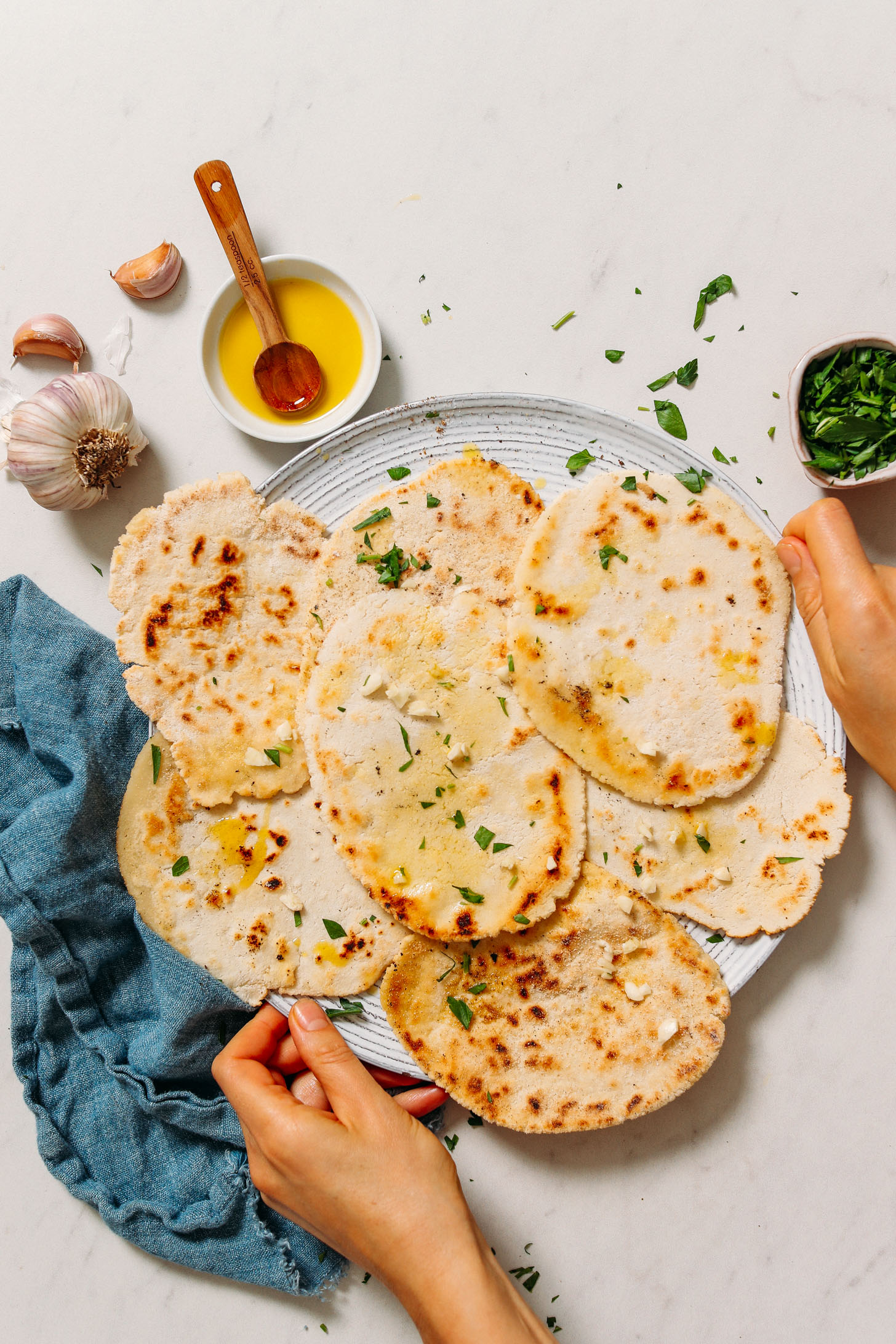 Holding a platter of gluten free naan topped with olive oil, garlic, and fresh parsley