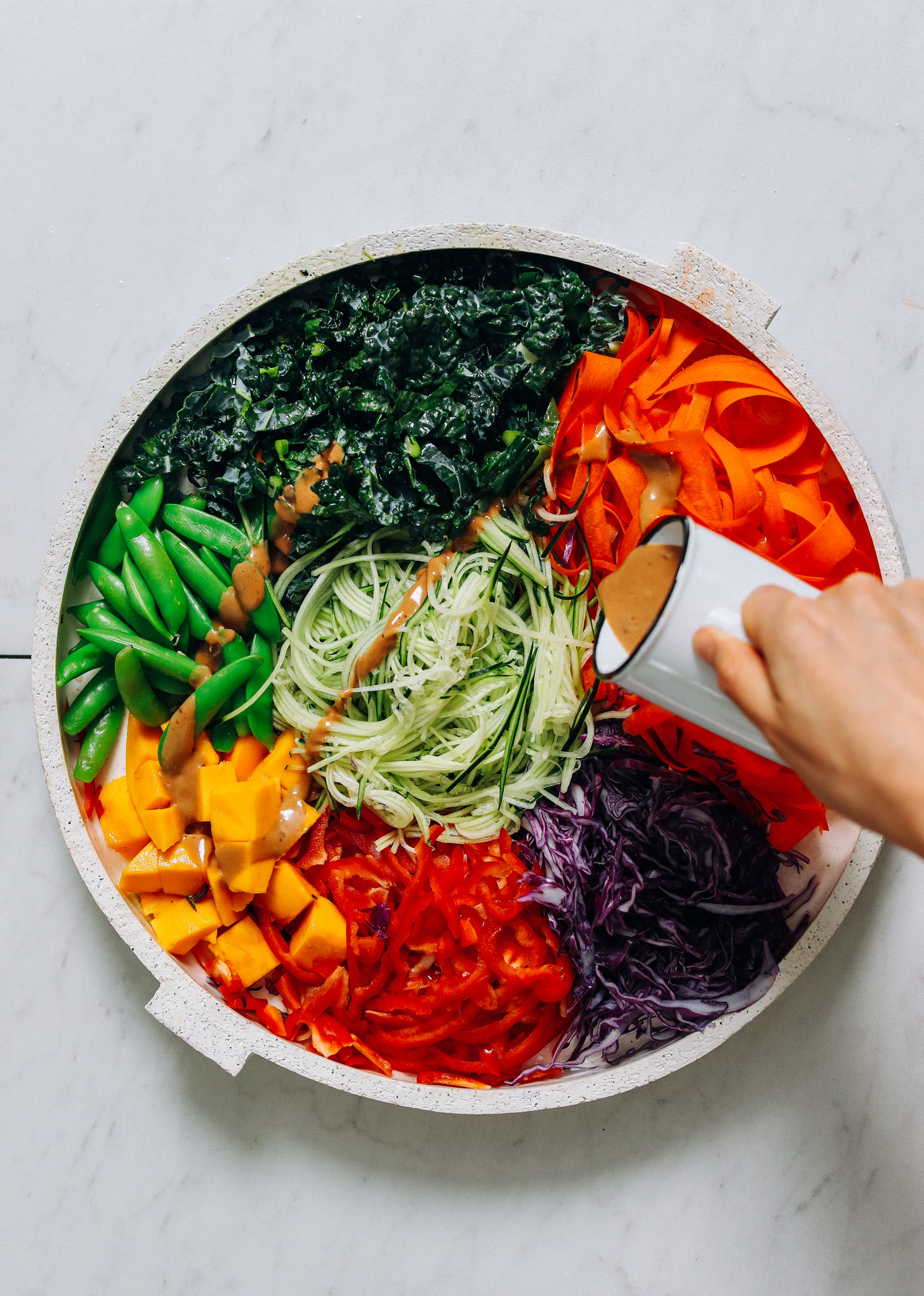 Pouring peanut sauce onto our Raw Peanut Noodle Salad