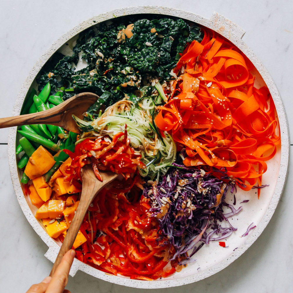 Using wooden tongs to pick up fresh vegetable noodle salad