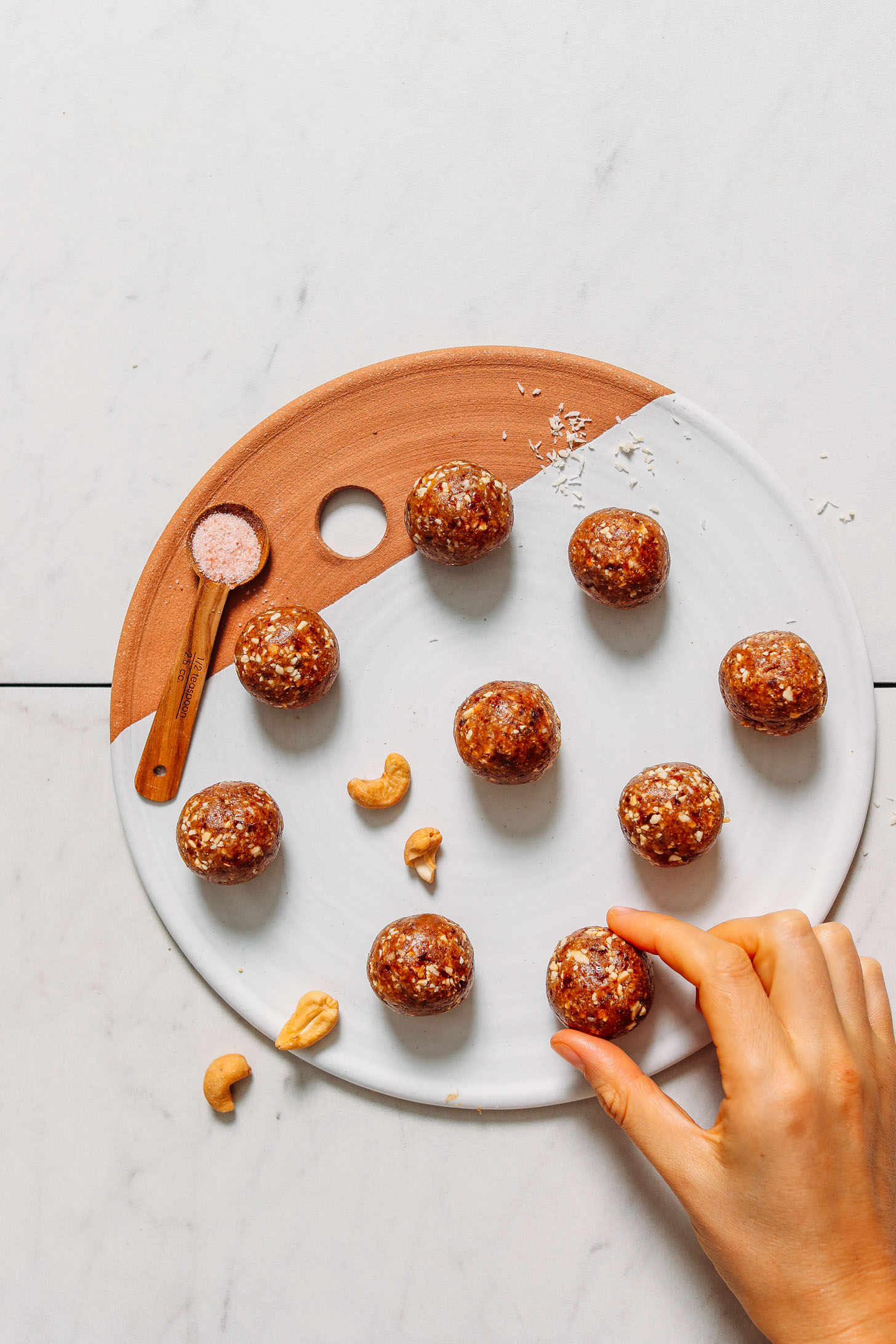 Clay and ceramic tray filled with date bites, sea salt, cashews, and shredded coconut