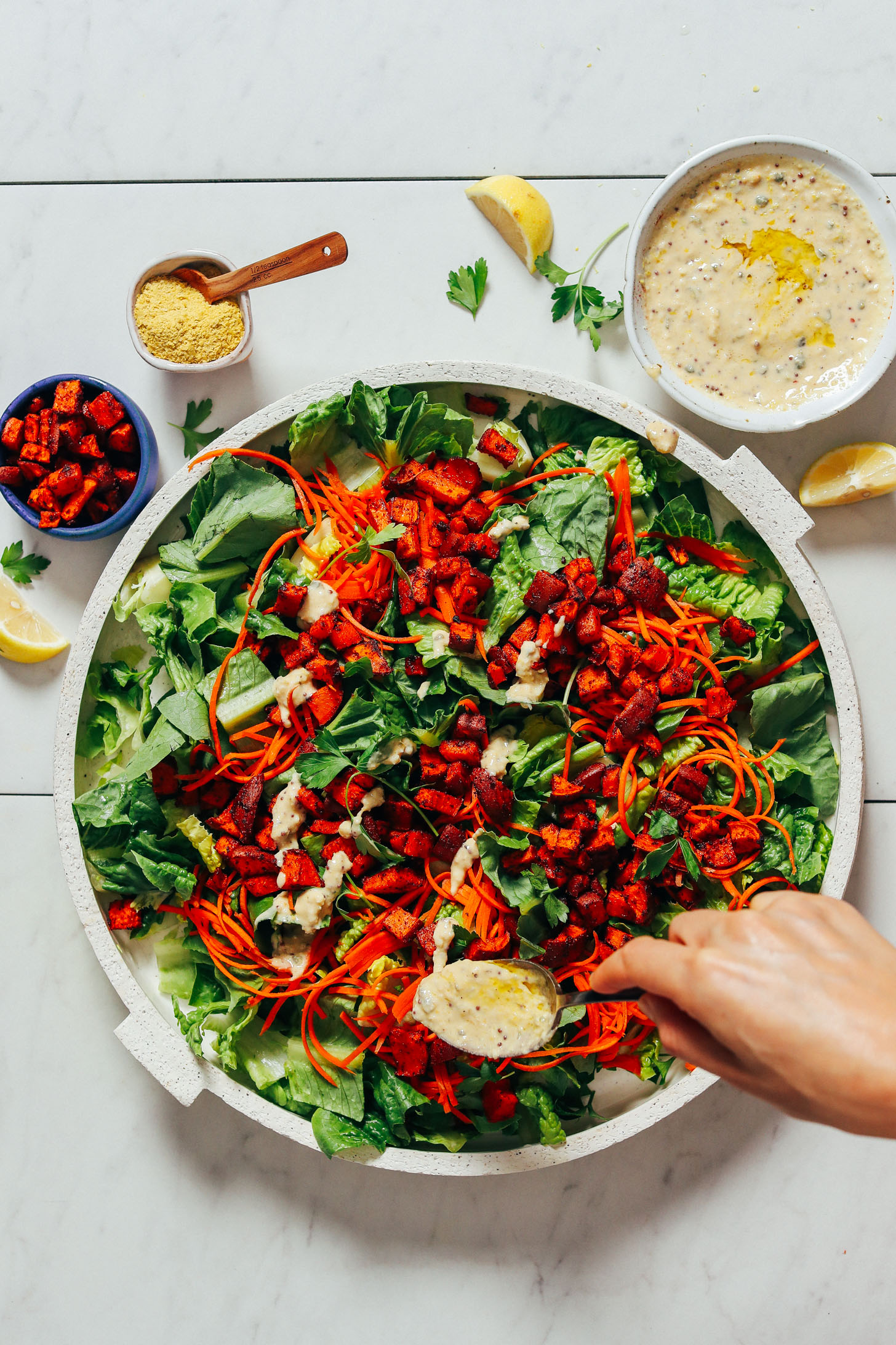 Using a spoon to drizzle Vegan Caesar Dressing onto a platter of salad