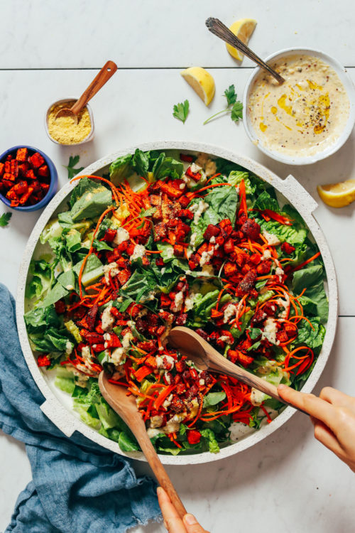 Using salad tongs to pick up a serving of Vegan Caesar Salad