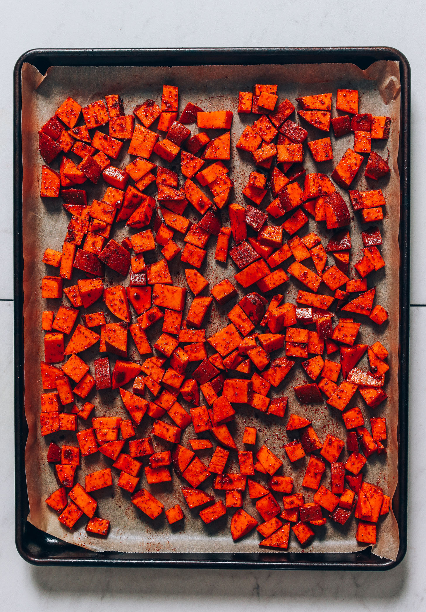 Baking sheet of cubed sweet potato tossed in oil and BBQ spices