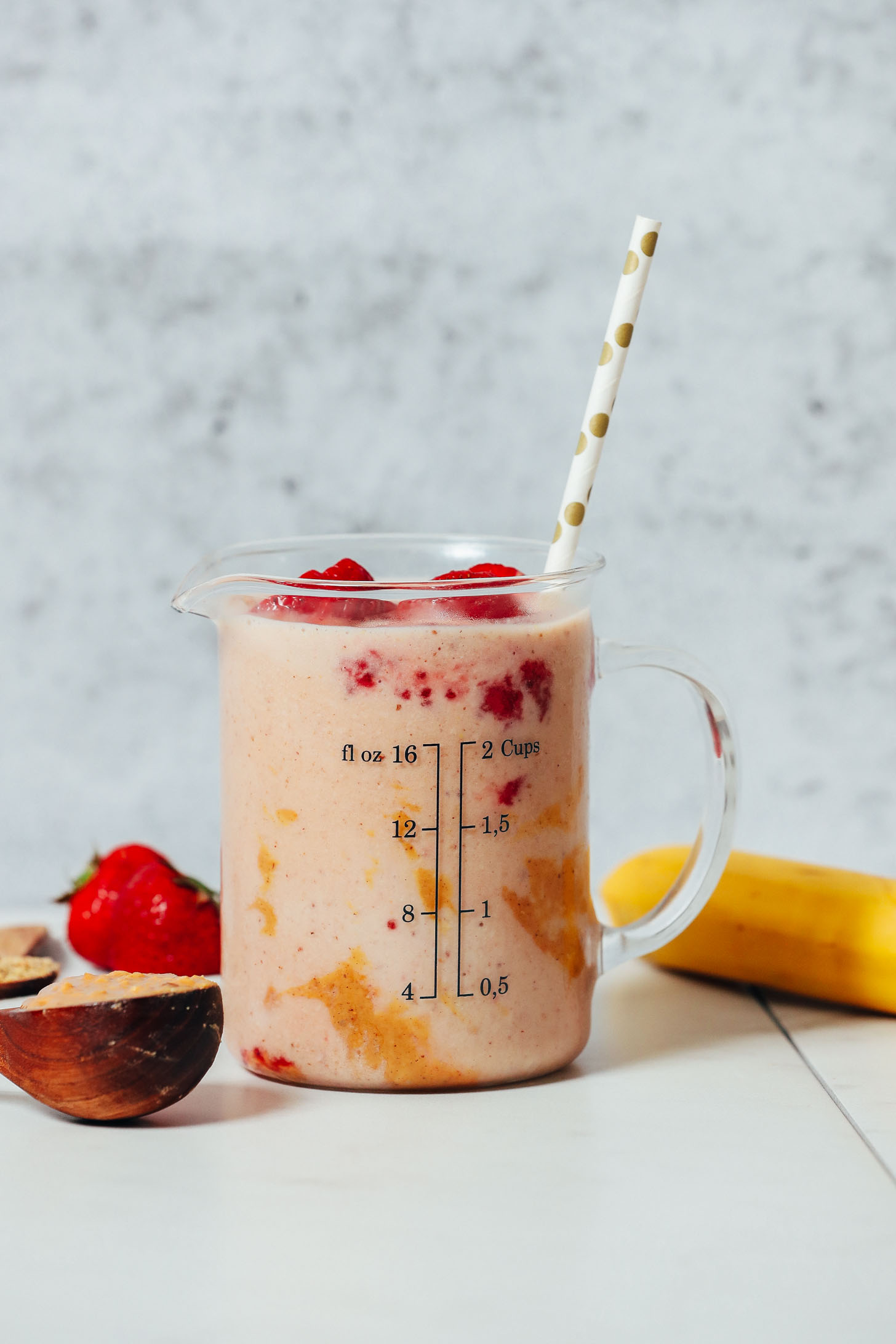 Measuring glass of our PB&J Smoothie next to peanut butter, strawberries, and a banana