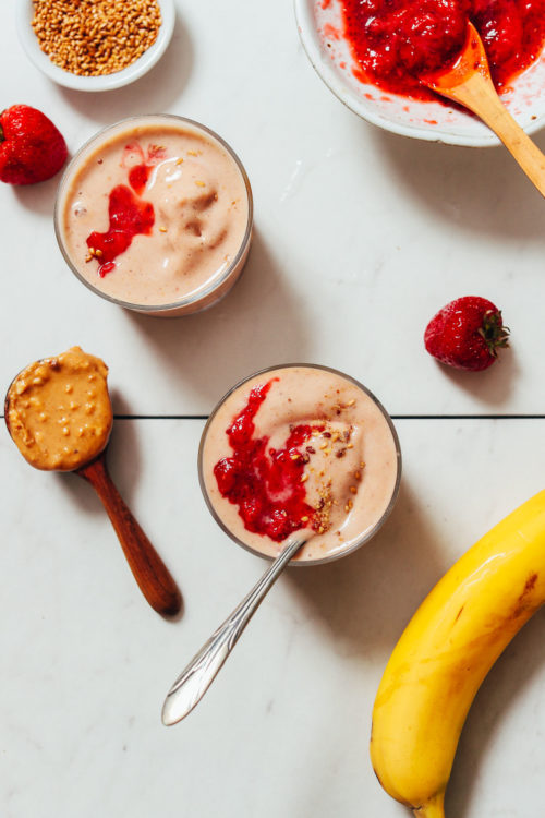 Top view of two glasses of our Peanut Butter and Jelly Smoothie next to ingredients used to make it