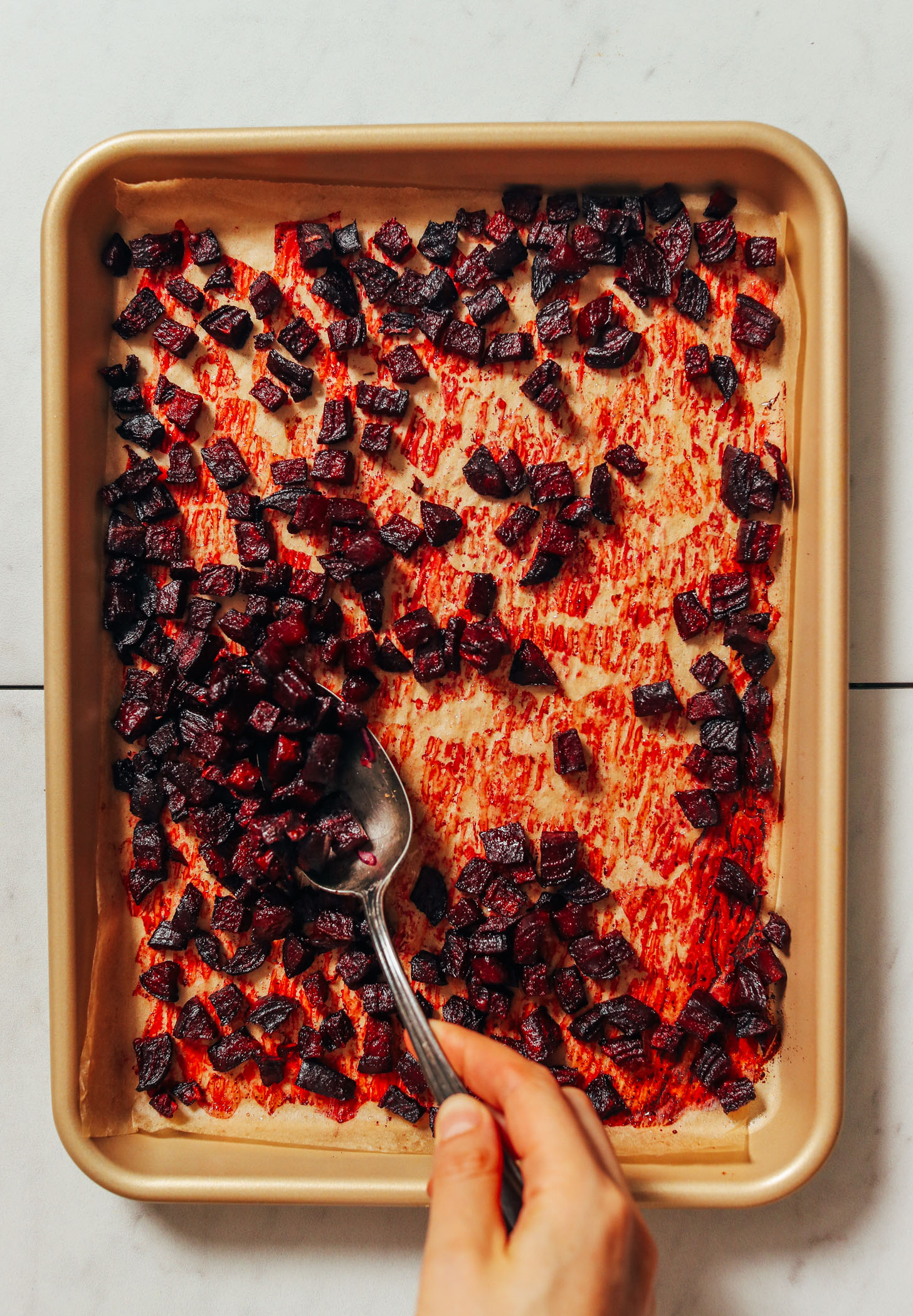 Using a spoon to pick up roasted cubed beets from a baking sheet