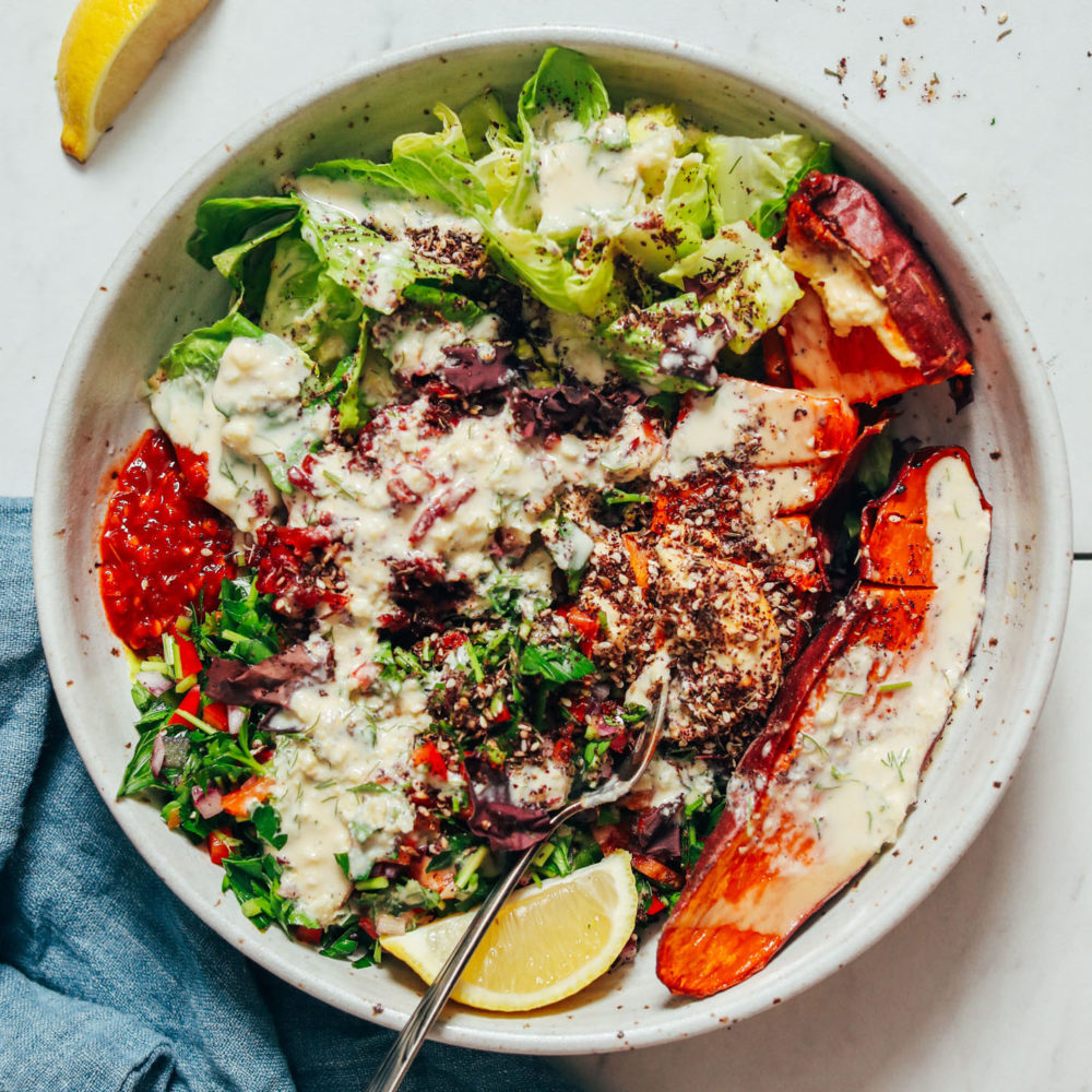 Nourish bowl with roasted sweet potato, romaine, parsley salad, dill garlic sauce, hummus, sauerkraut, tahini, and za'atar
