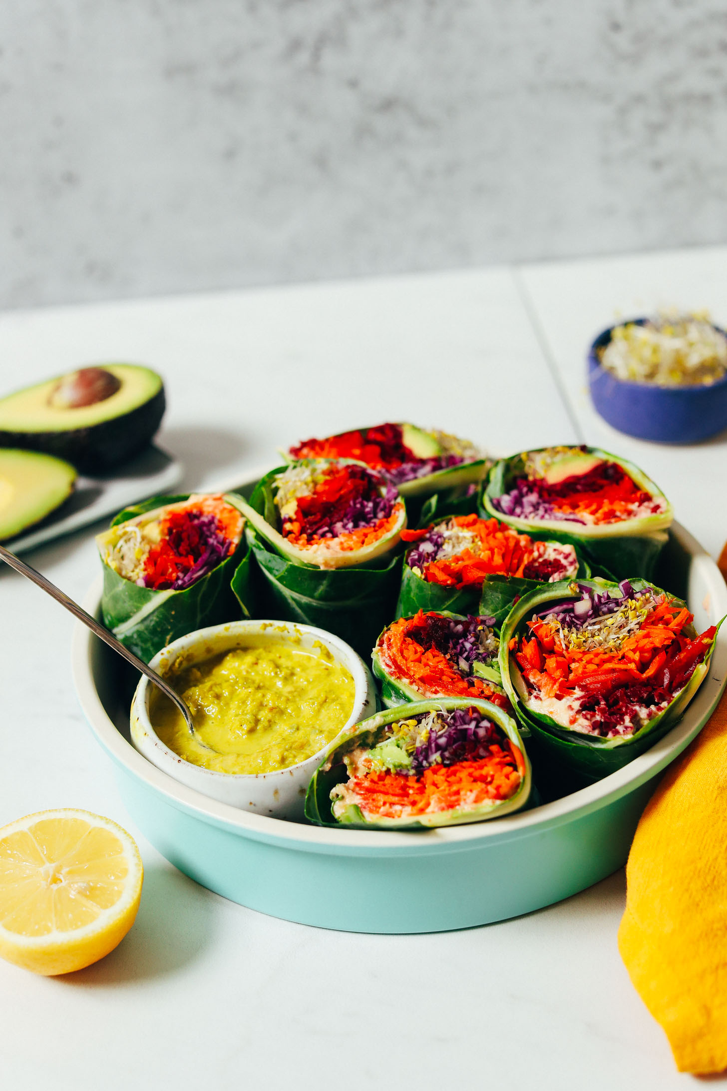 Avocado, broccoli sprouts, lemon, and green curry tahini sauce next to collard wraps