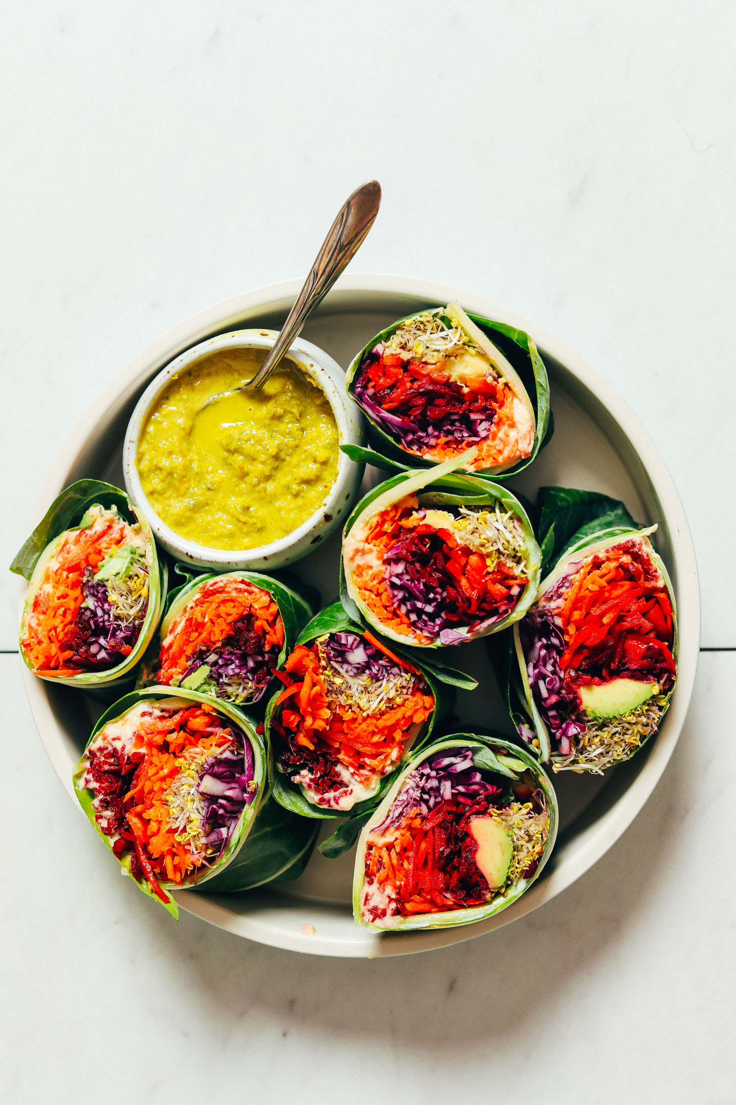 Bowl of green curry tahini sauce next to fresh vegetable collard green wraps