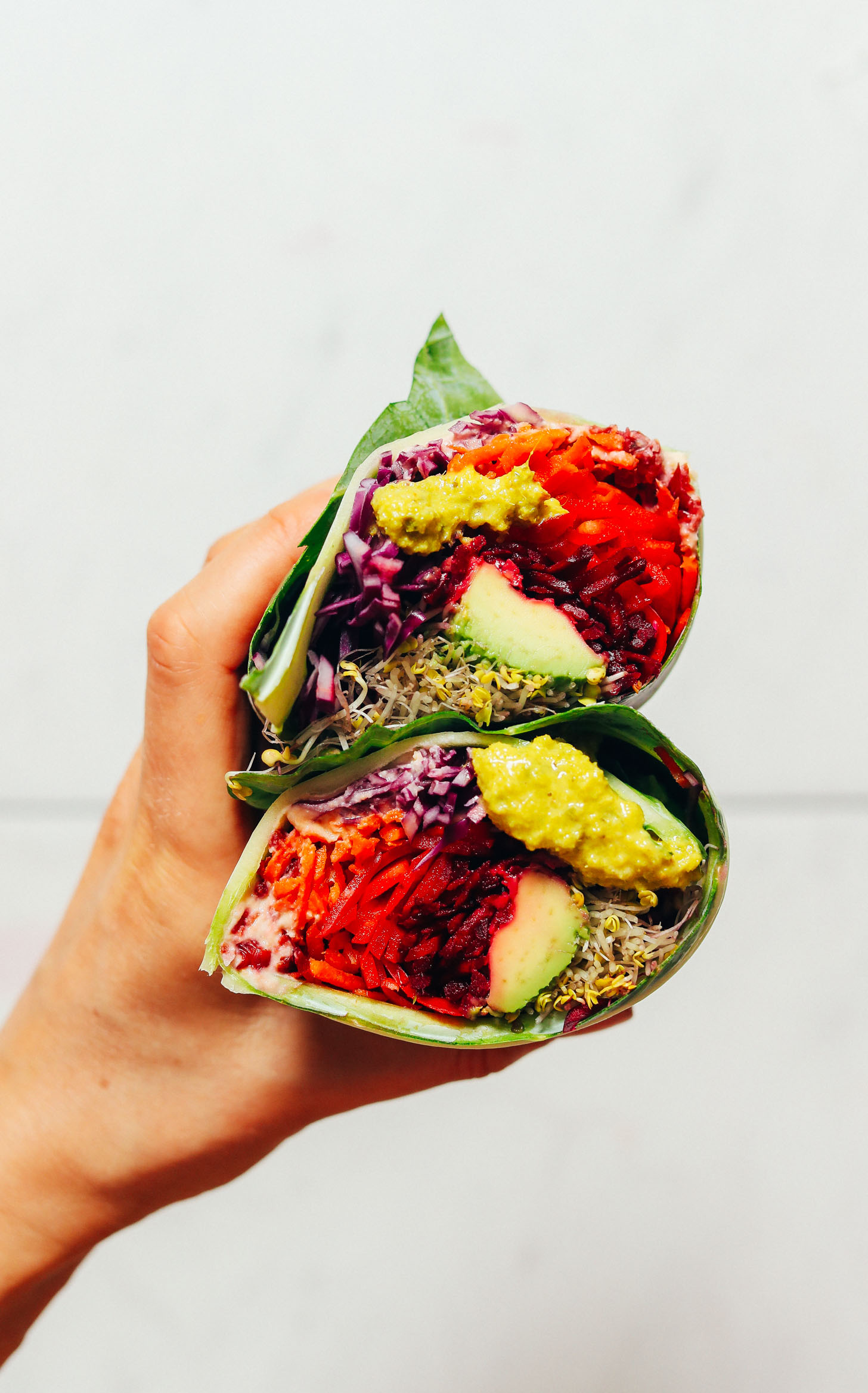 Holding up a Collard Wrap filled with fresh veggies and green curry tahini sauce