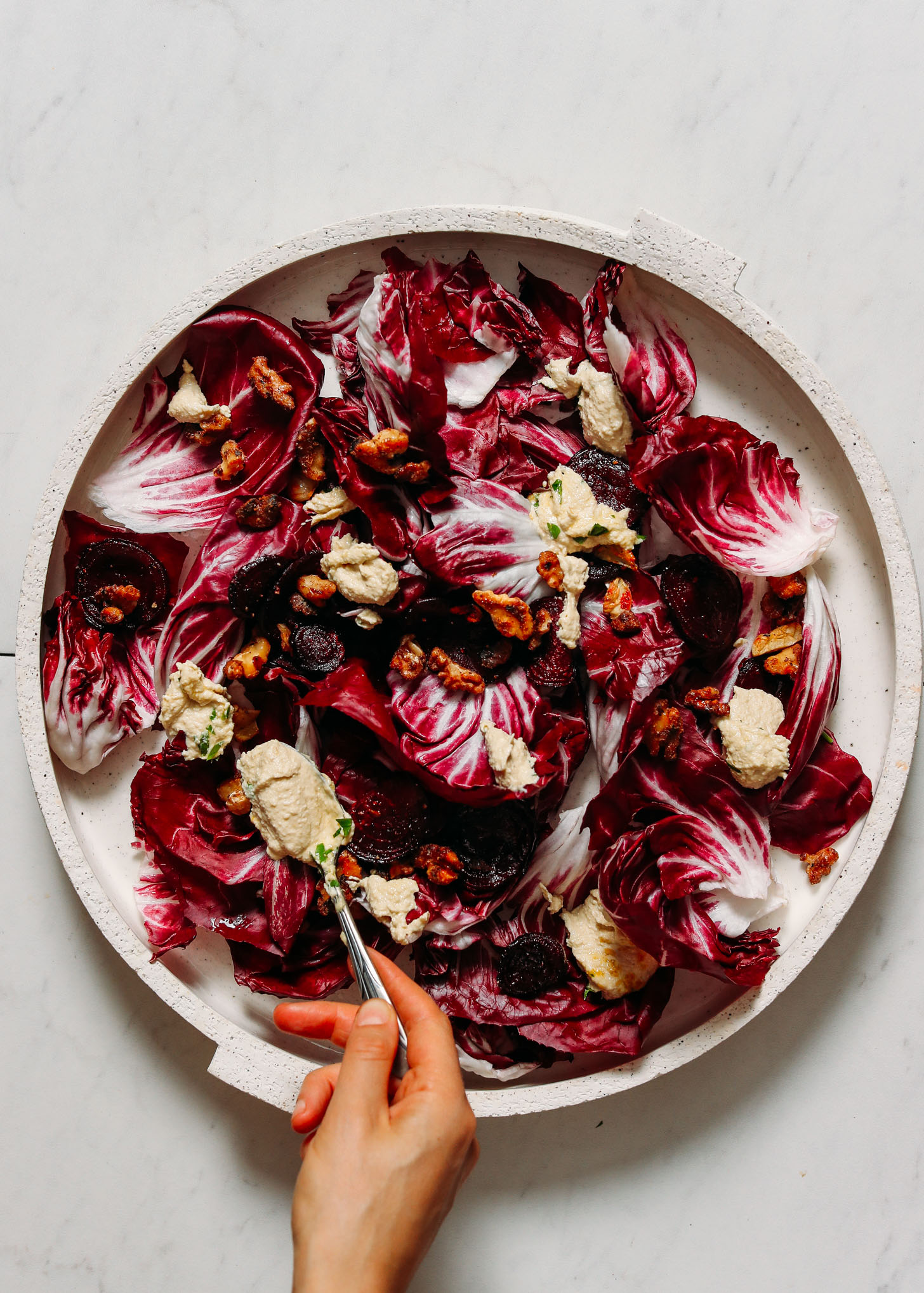 Using a spoon to spread ricotta dressing over a salad