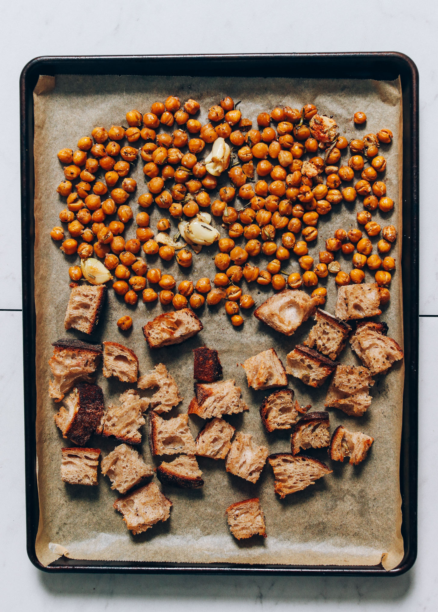 Parchment-lined baking sheet of crusty bread, garlic cloves, and chickpeas