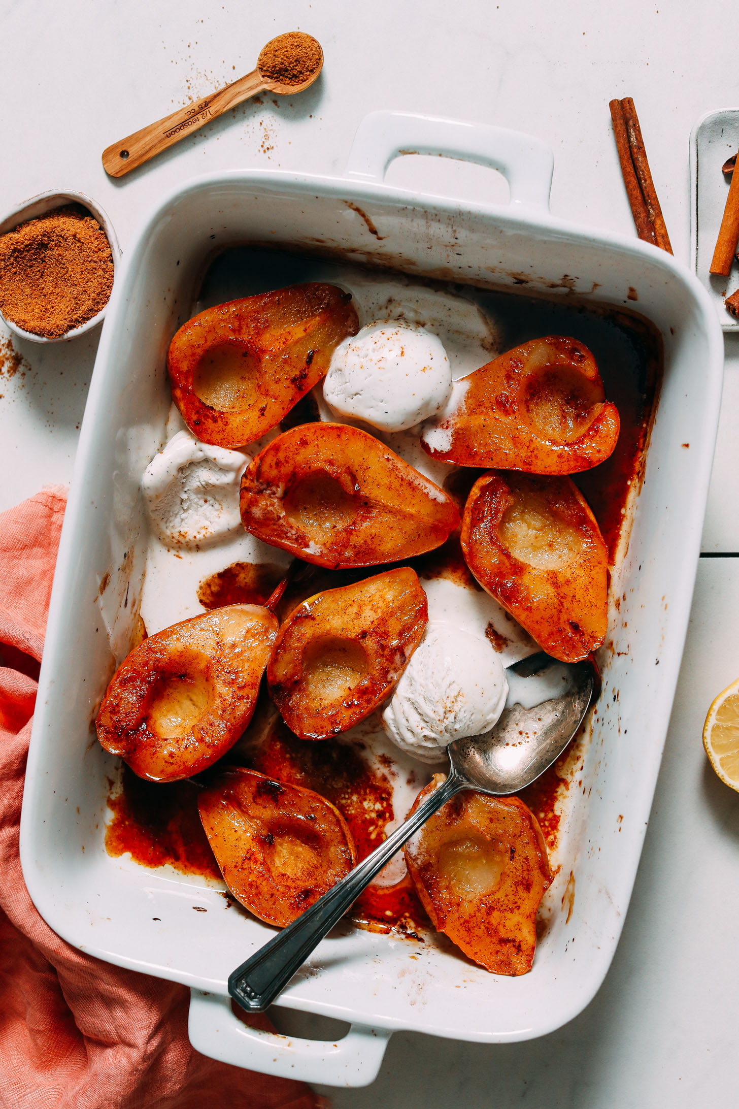 Perfectly baked pear halves in a white baking dish with scoops of vegan ice cream