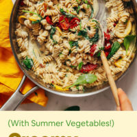 Stirring a pan of Creamy Vegan Pasta with squash, roasted tomatoes, and spinach
