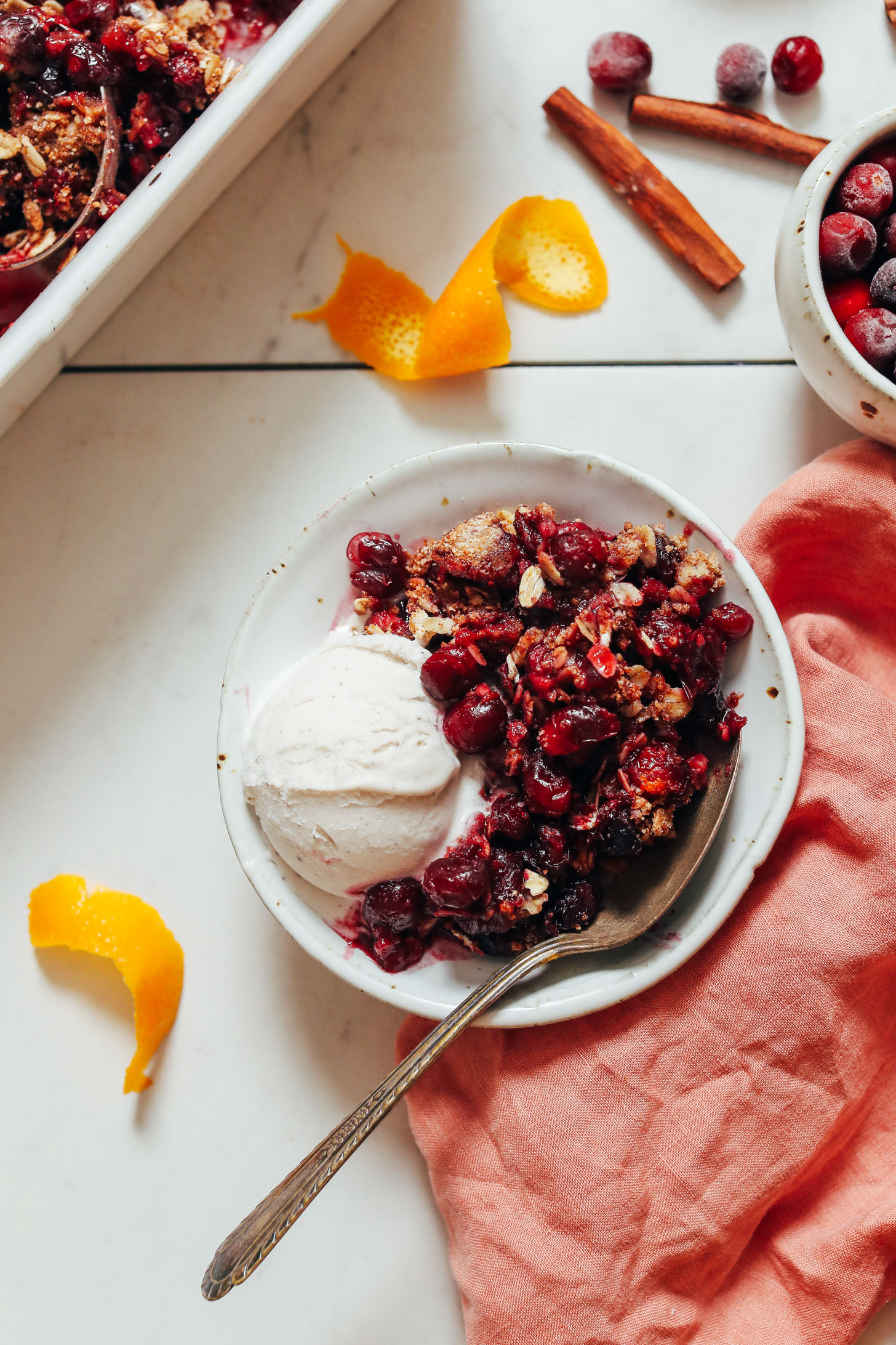 Spoon in a bowl of gluten-free cranberry crisp with vegan vanilla ice cream