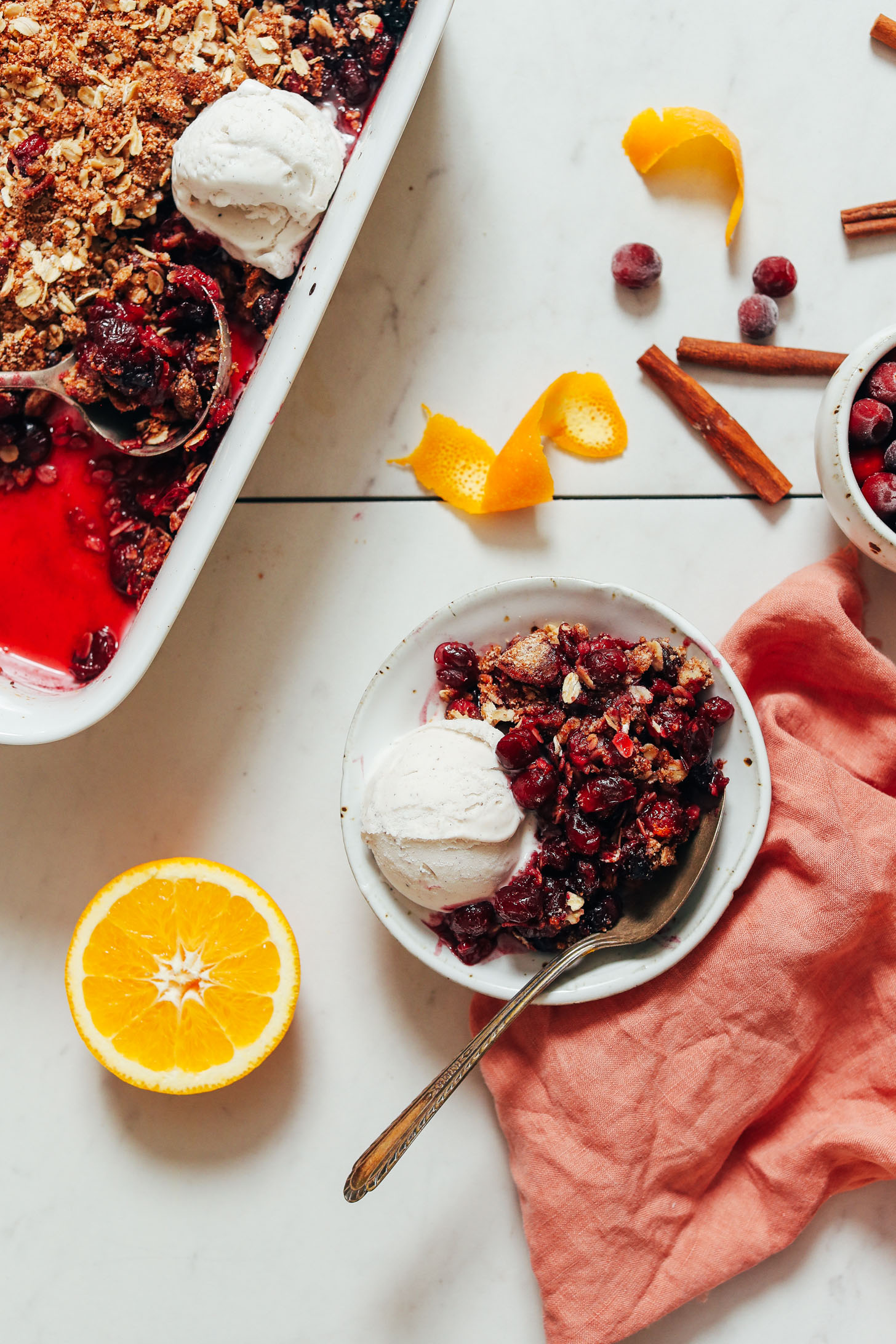 Bowl and baking dish of orange cranberry crisp with vegan vanilla ice cream