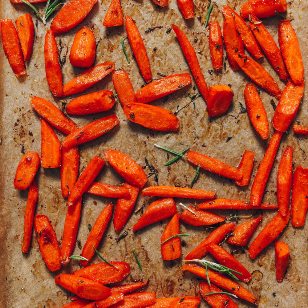 Baking sheet of perfect roasted carrots with fresh rosemary and thyme