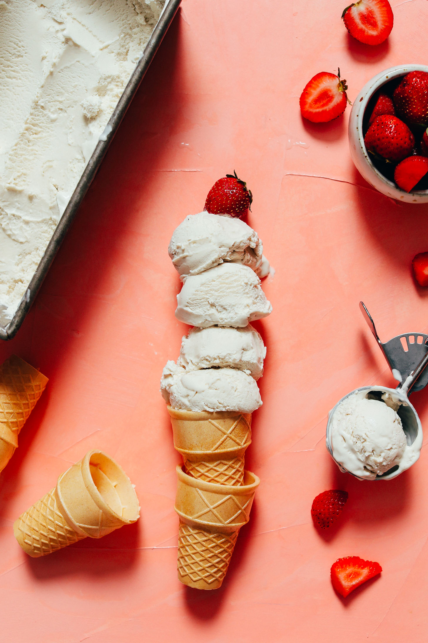 Bowl of strawberries next to scoops and pan of creamy vegan vanilla ice cream