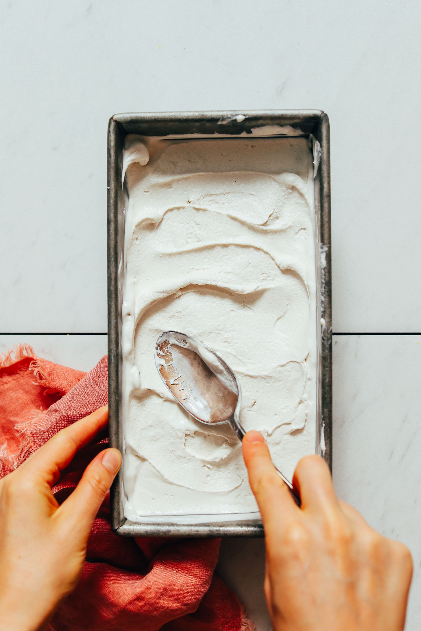 Using a spoon to smooth out a pan of homemade vegan vanilla ice cream