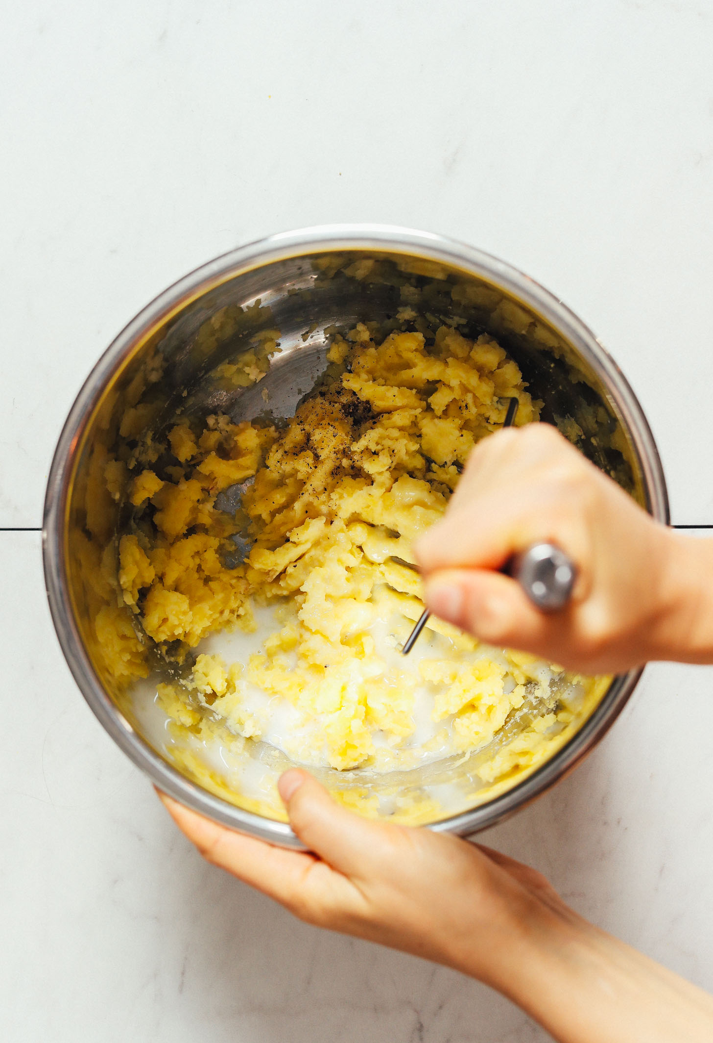 Using a potato masher to mash potatoes with vegan butter and dairy-free milk