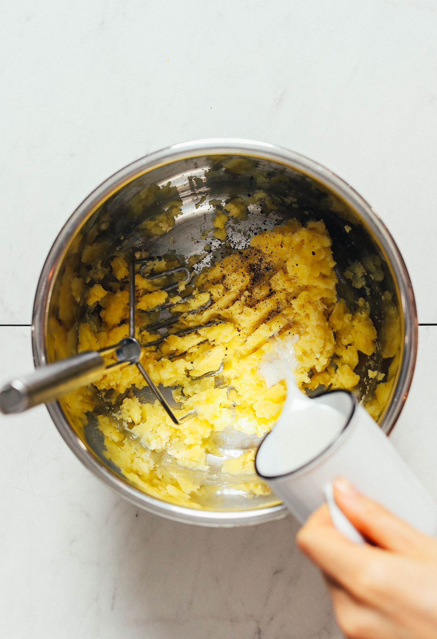 Pouring dairy-free milk into a pot to make mashed potatoes