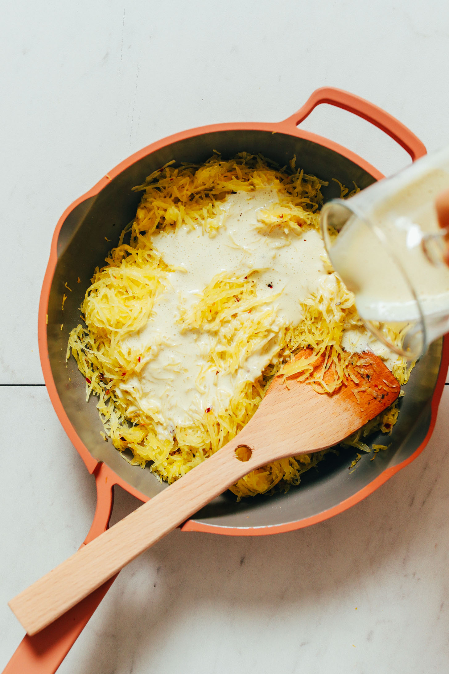 Pouring vegan alfredo sauce into a pan of spaghetti squash noodles