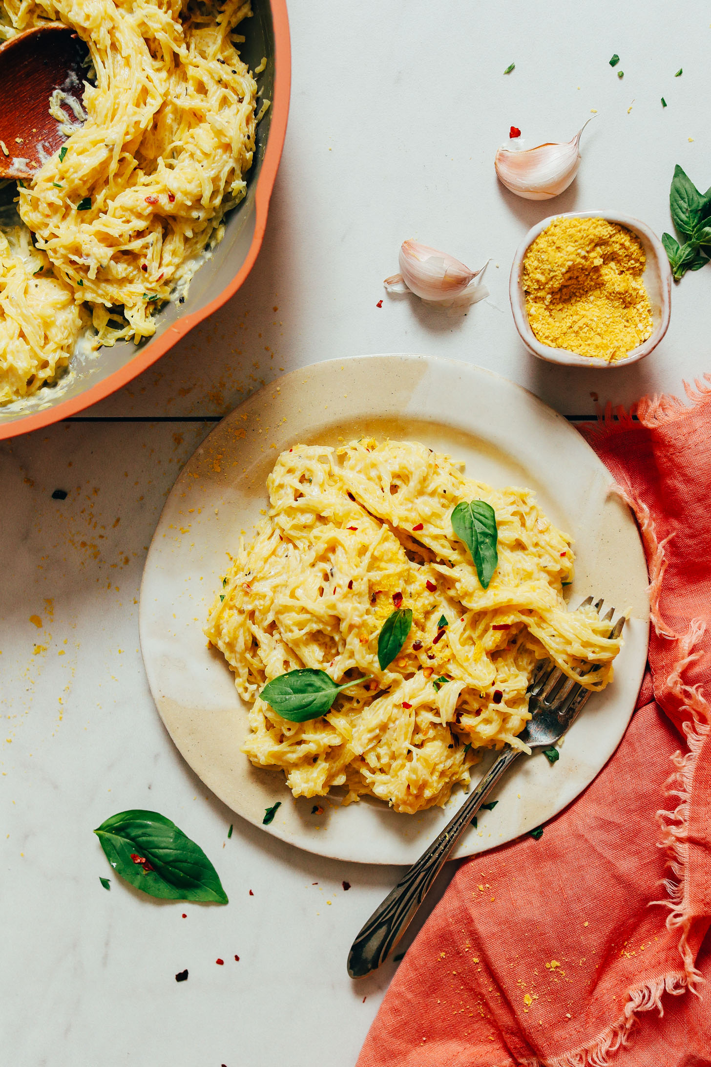 Nutritional yeast, garlic cloves, and pan and plate of spaghetti squash pasta with garlicky alfredo