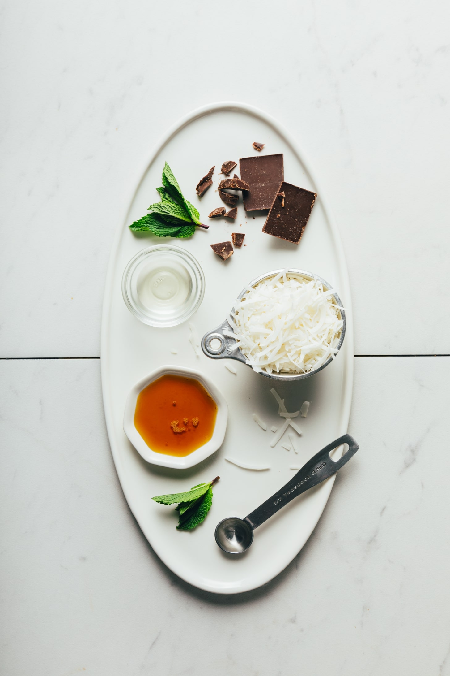 Tray of dark chocolate, shredded coconut, coconut oil, maple syrup, and fresh mint