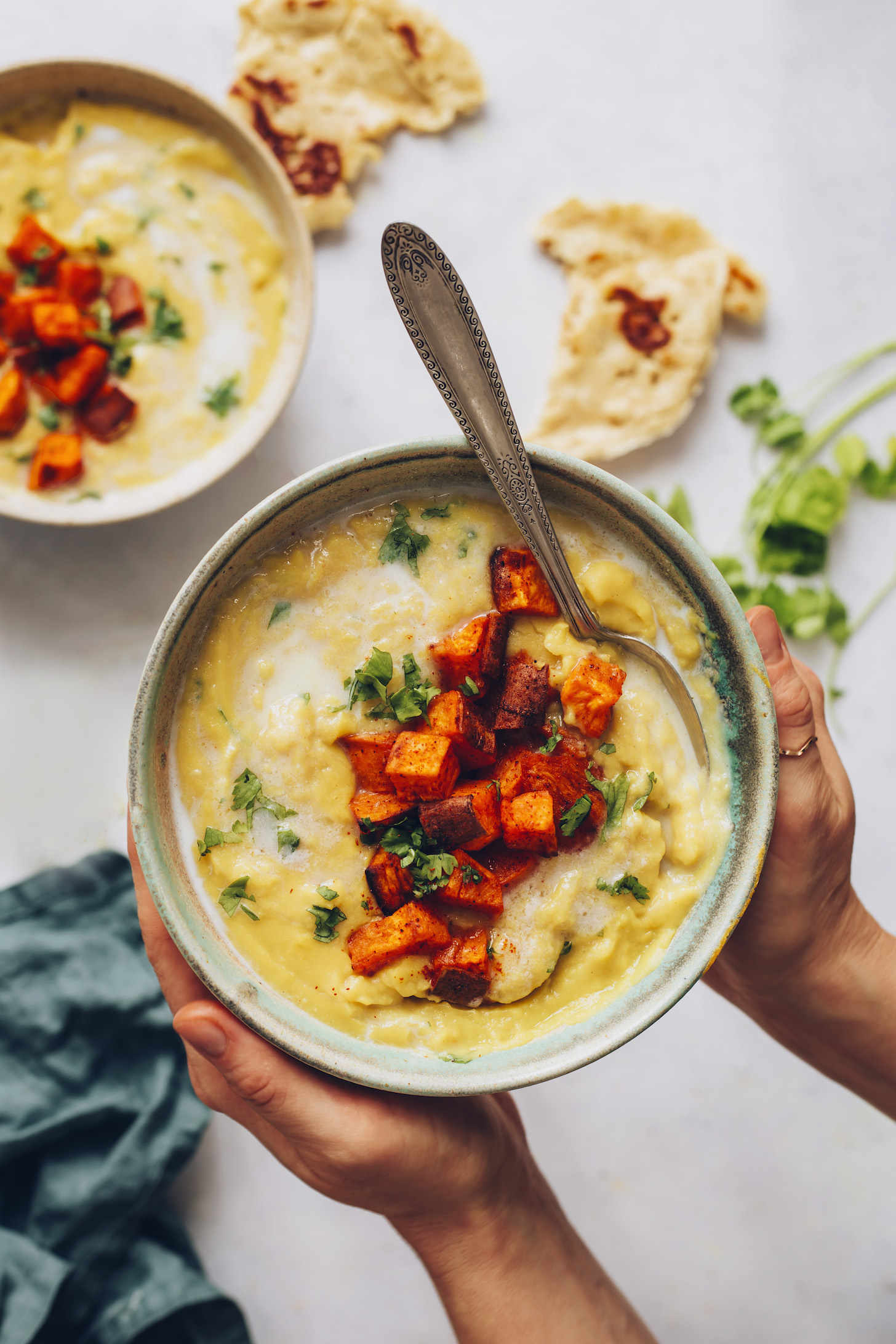 Holding a bowl of yellow split pea soup topped with roasted sweet potato and cilantro