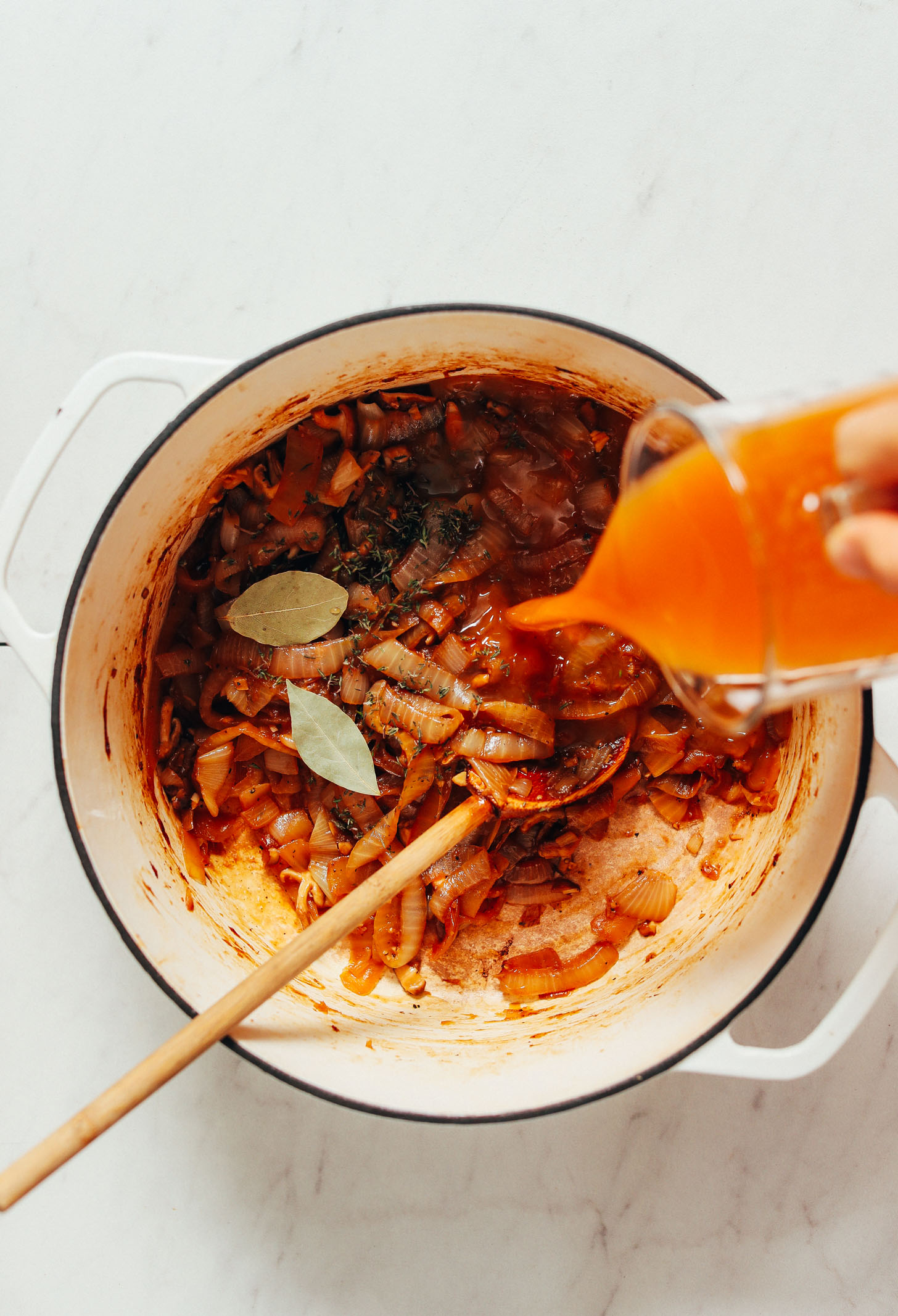 Pouring vegetable broth over caramelized onions and herbs