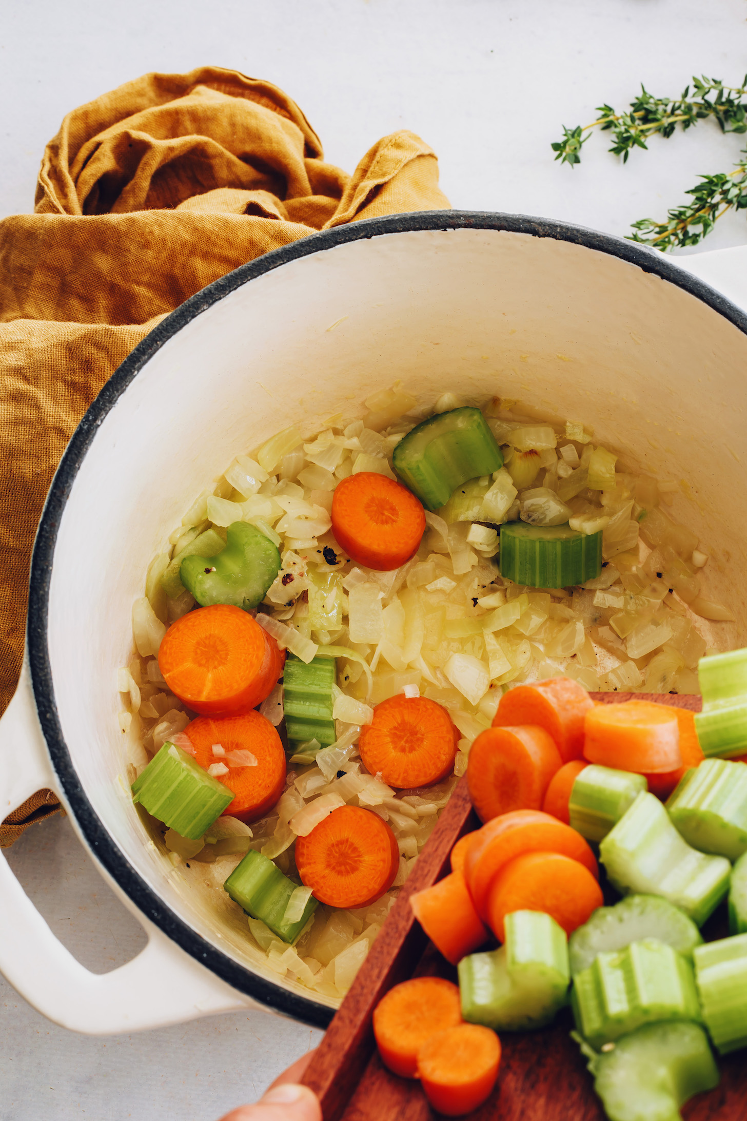 Pouring carrot and celery into a pot of sautéed onion
