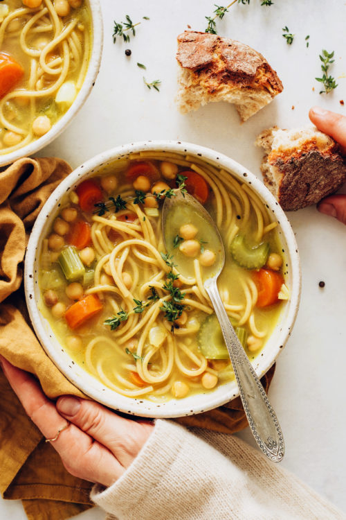 Hands holding a bowl of chicken noodle soup