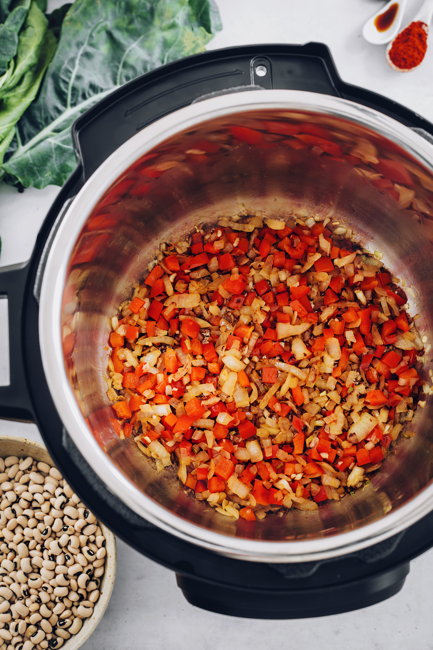 Bowl of black eyed peas next to an Instant Pot of sautéed onion and bell pepper