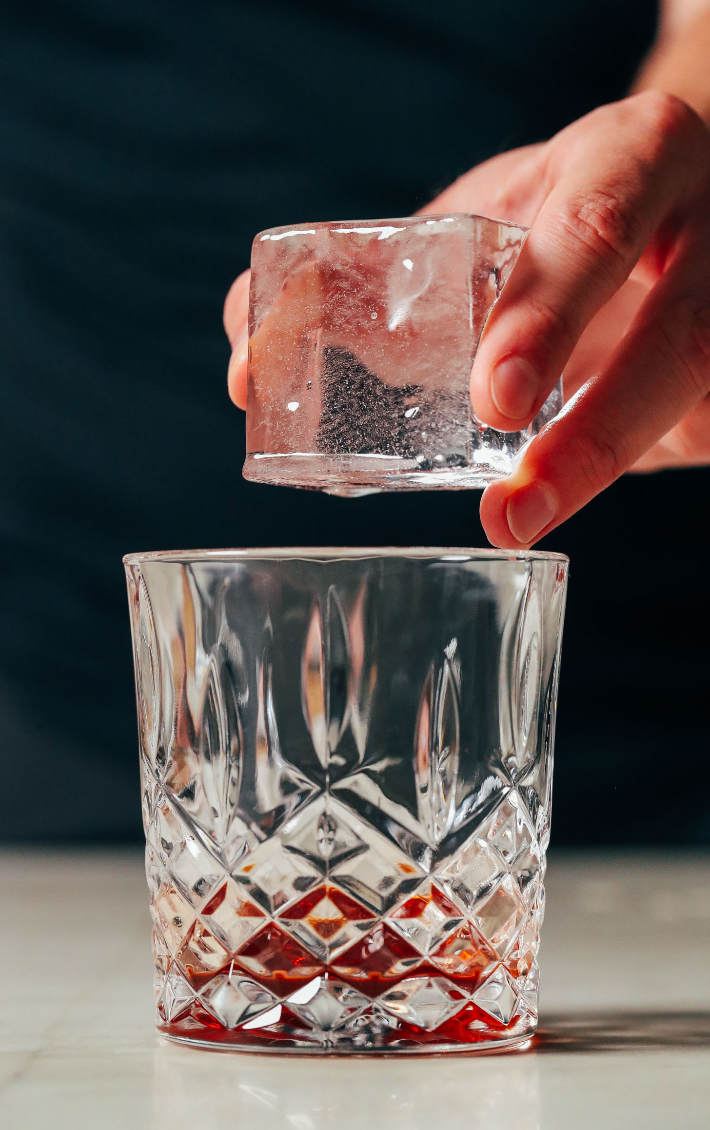 Adding a clear ice cube to a glass of bitters