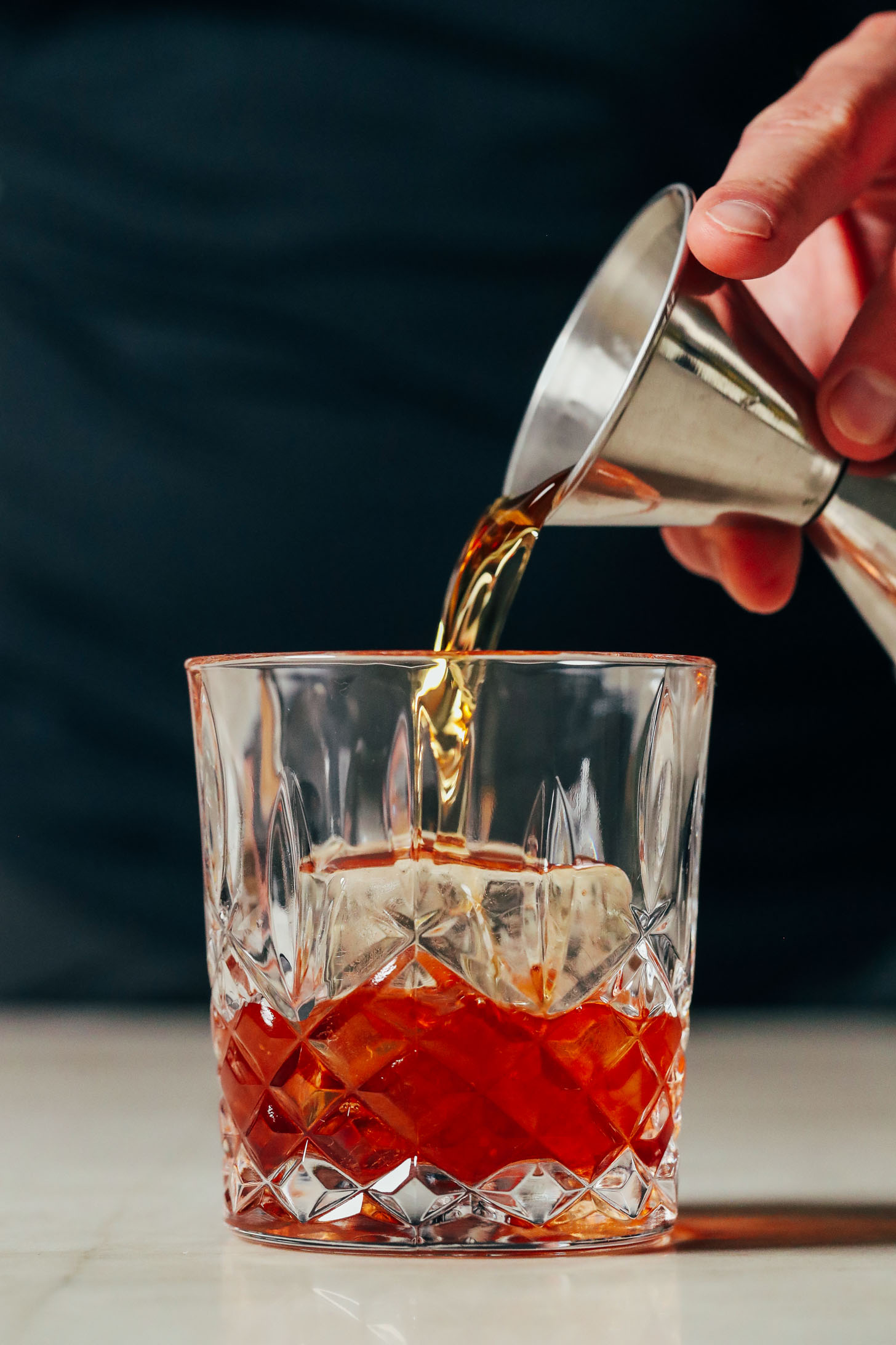 Pouring bourbon over a clear ice cube in a glass