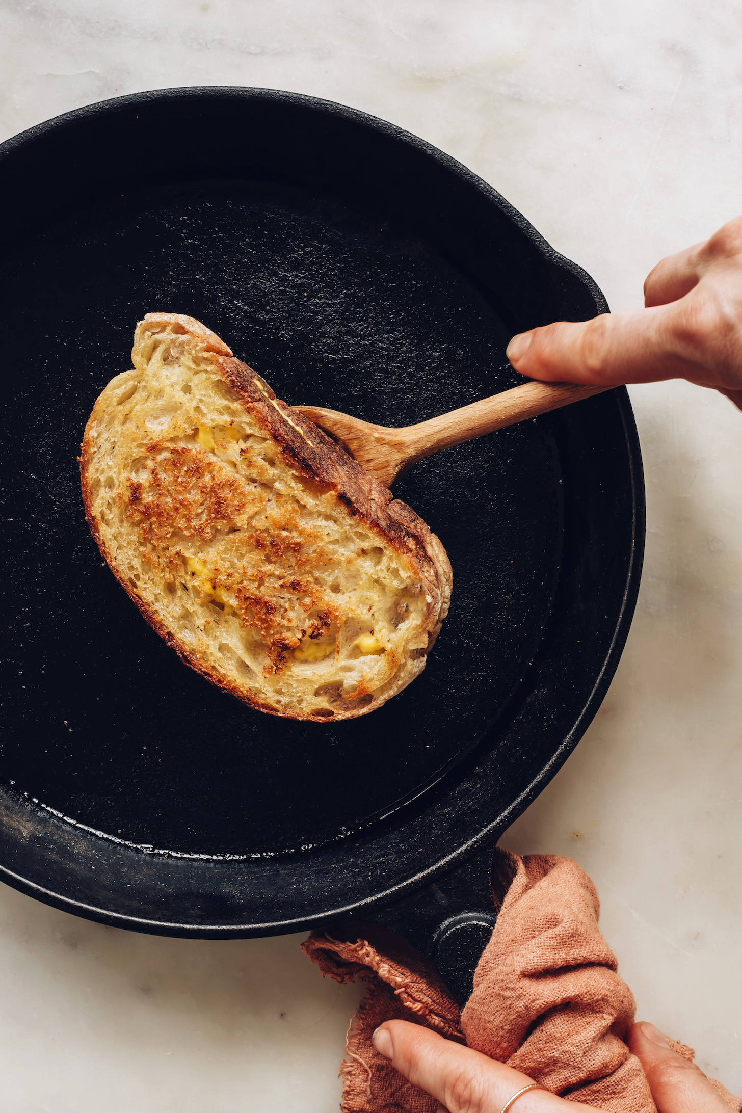 Using a wooden spoon to flip a vegan grilled cheese in a cast iron pan