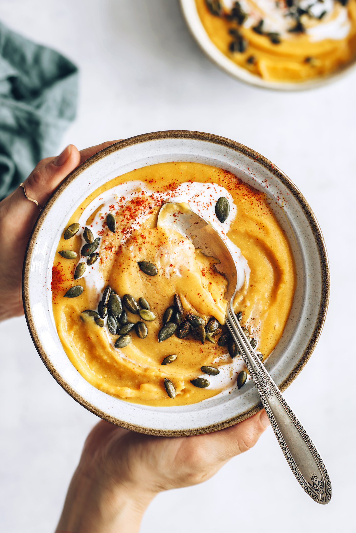 Holding a bowl of creamy sweet potato red lentil soup topped with pepitas