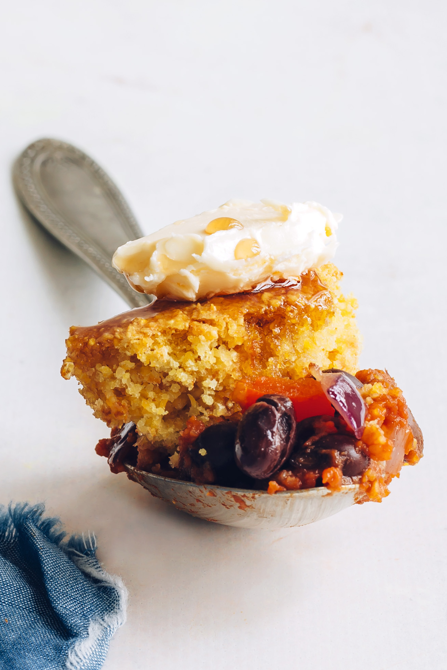 Spoonful of black bean enchilada skillet with cornbread topping, vegan butter, and maple syrup