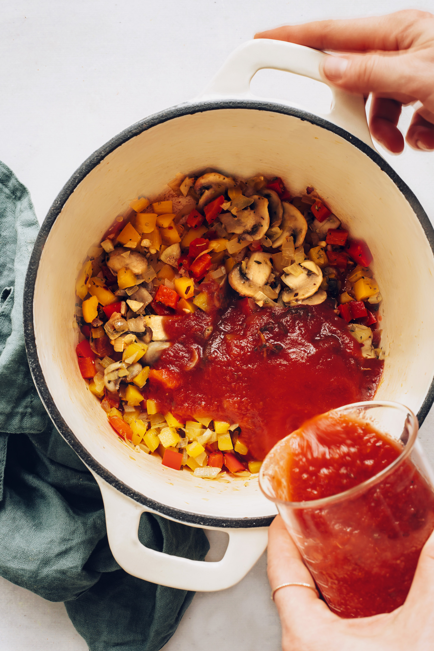 Pouring marinara sauce into a pot of sautéed vegetables