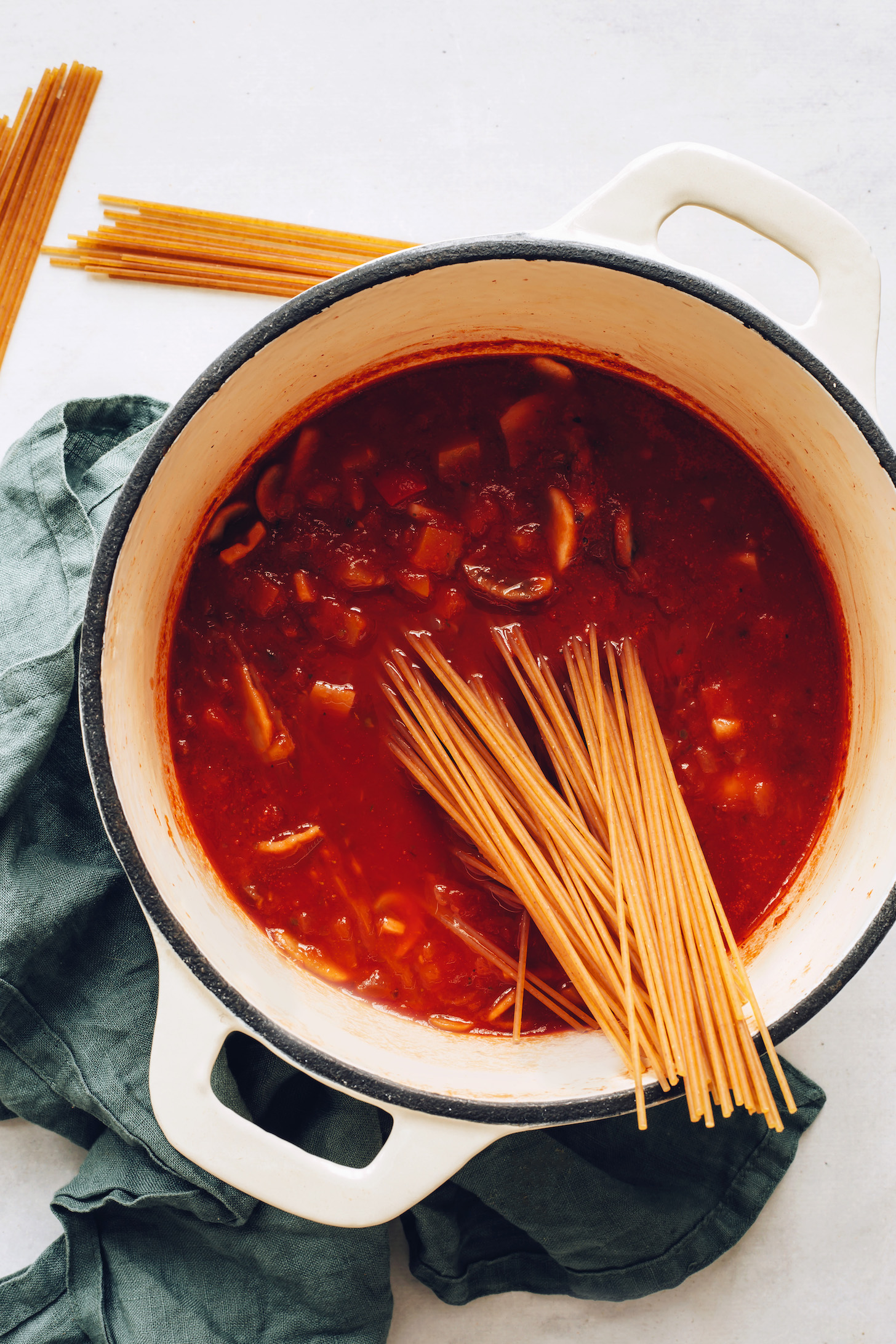 Uncooked spaghetti noodles resting in a pot of hearty marinara