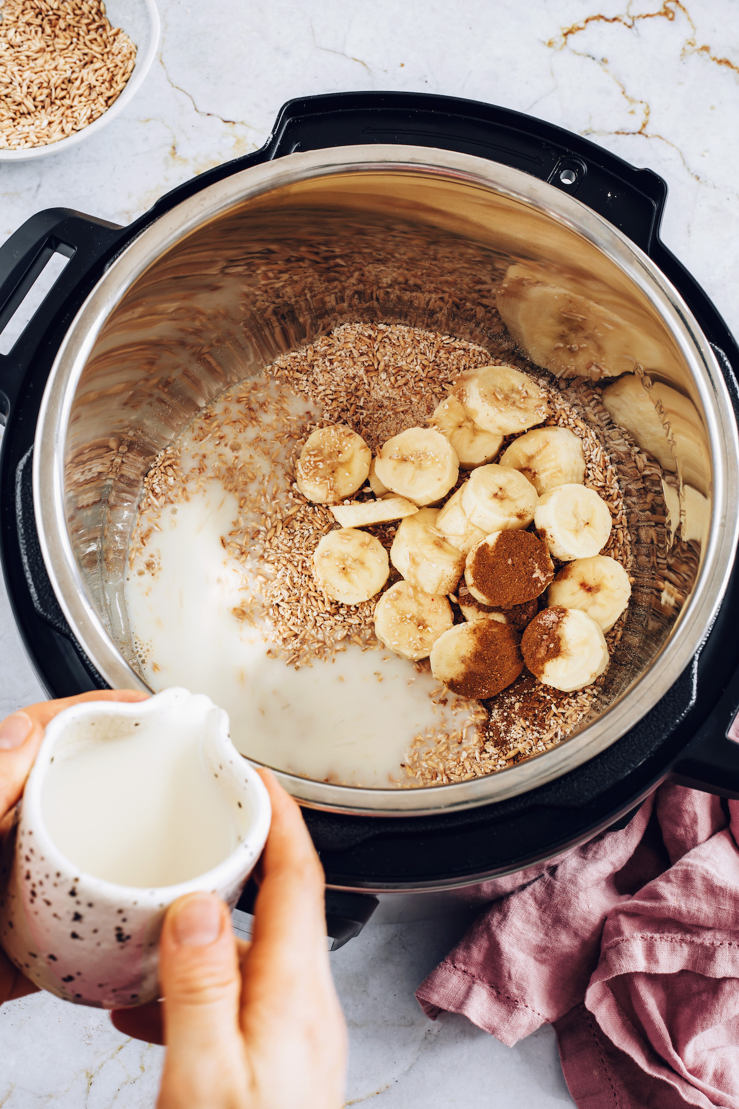 Pouring dairy-free milk over steel cut oats, banana, and cinnamon