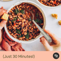 Spoon in a bowl of vegan hoppin john black eyed beans and greens