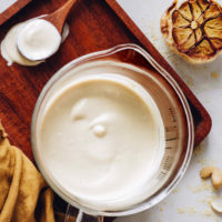 Roasted garlic next to a spoon and jar of creamy vegan bechamel sauce
