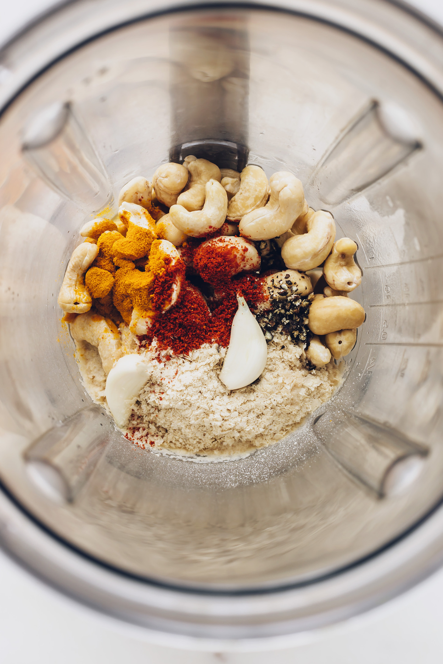 Blender with cashews, garlic, nutritional yeast, chili powder, turmeric, salt, and pepper