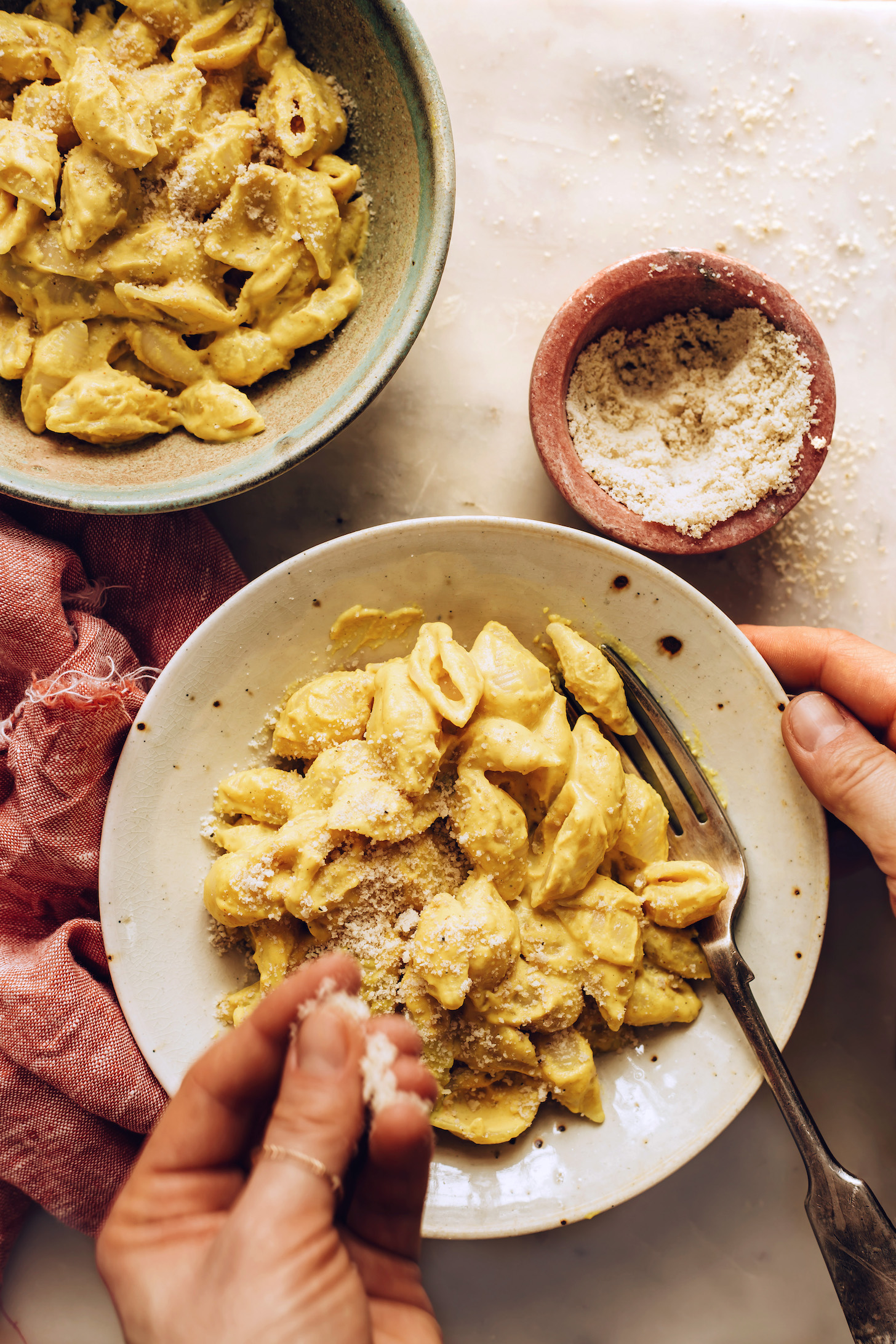 Sprinkling vegan parmesan cheese over a bowl of vegan mac and cheese
