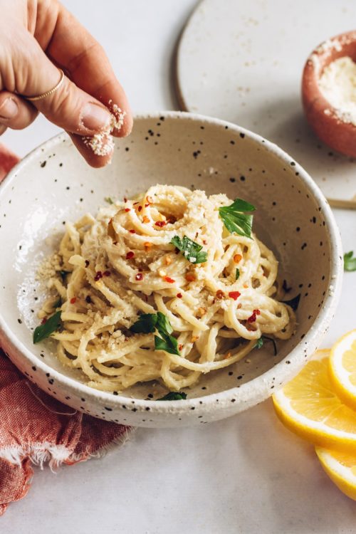 Sprinkling vegan parmesan cheese onto a bowl of pasta al limone