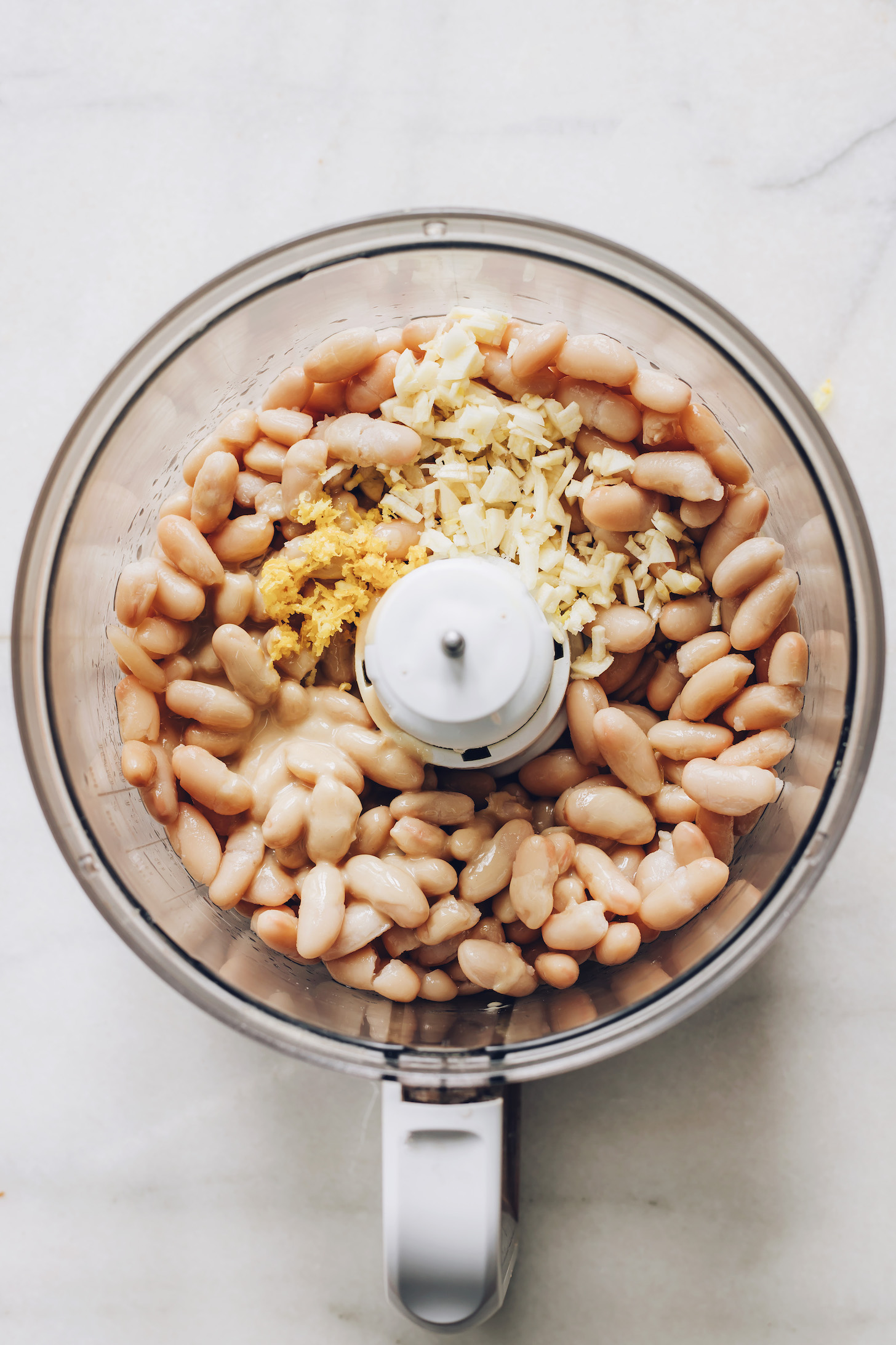 Food processor with white beans, garlic, and lemon zest