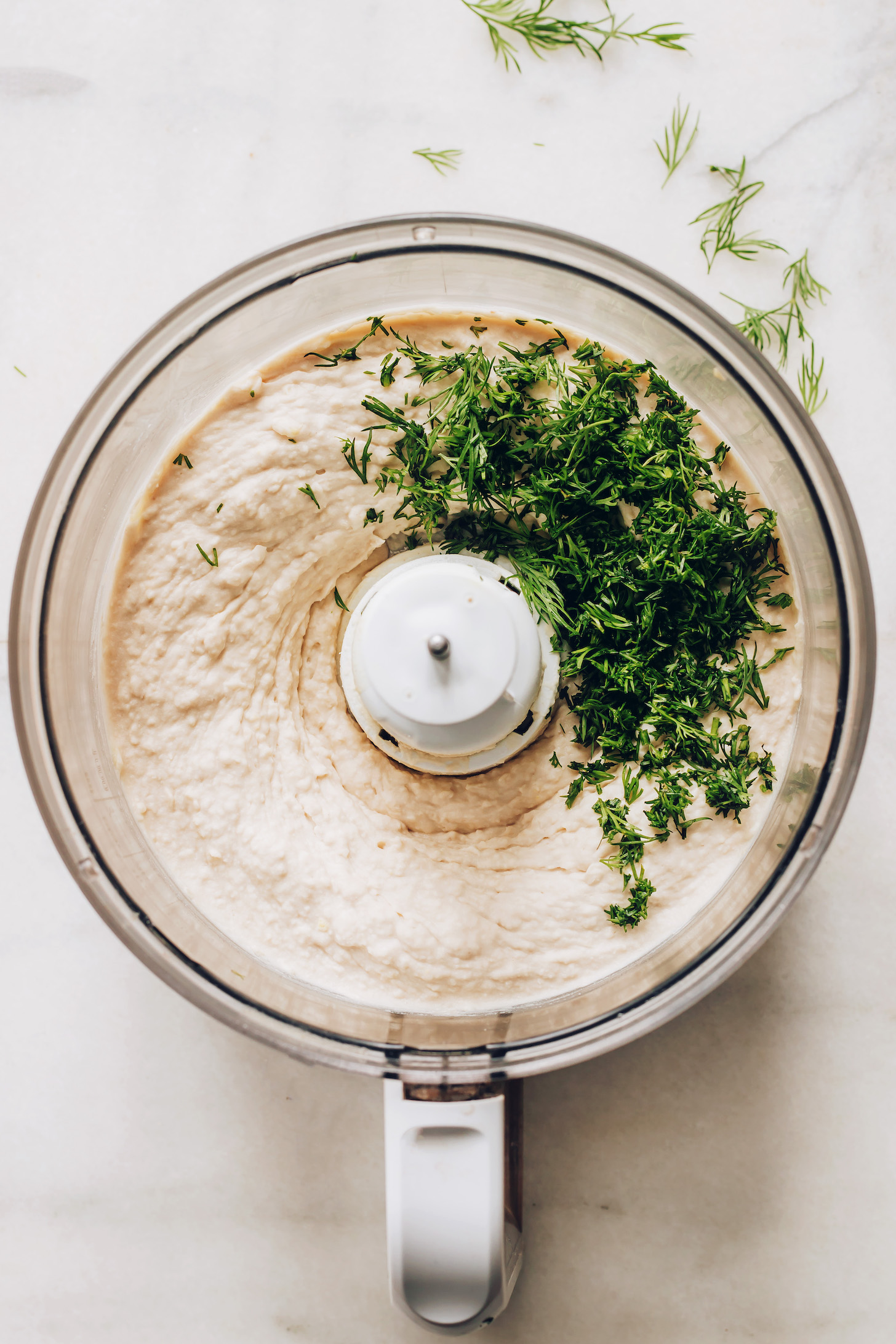 Food processor of white bean hummus topped with fresh dill